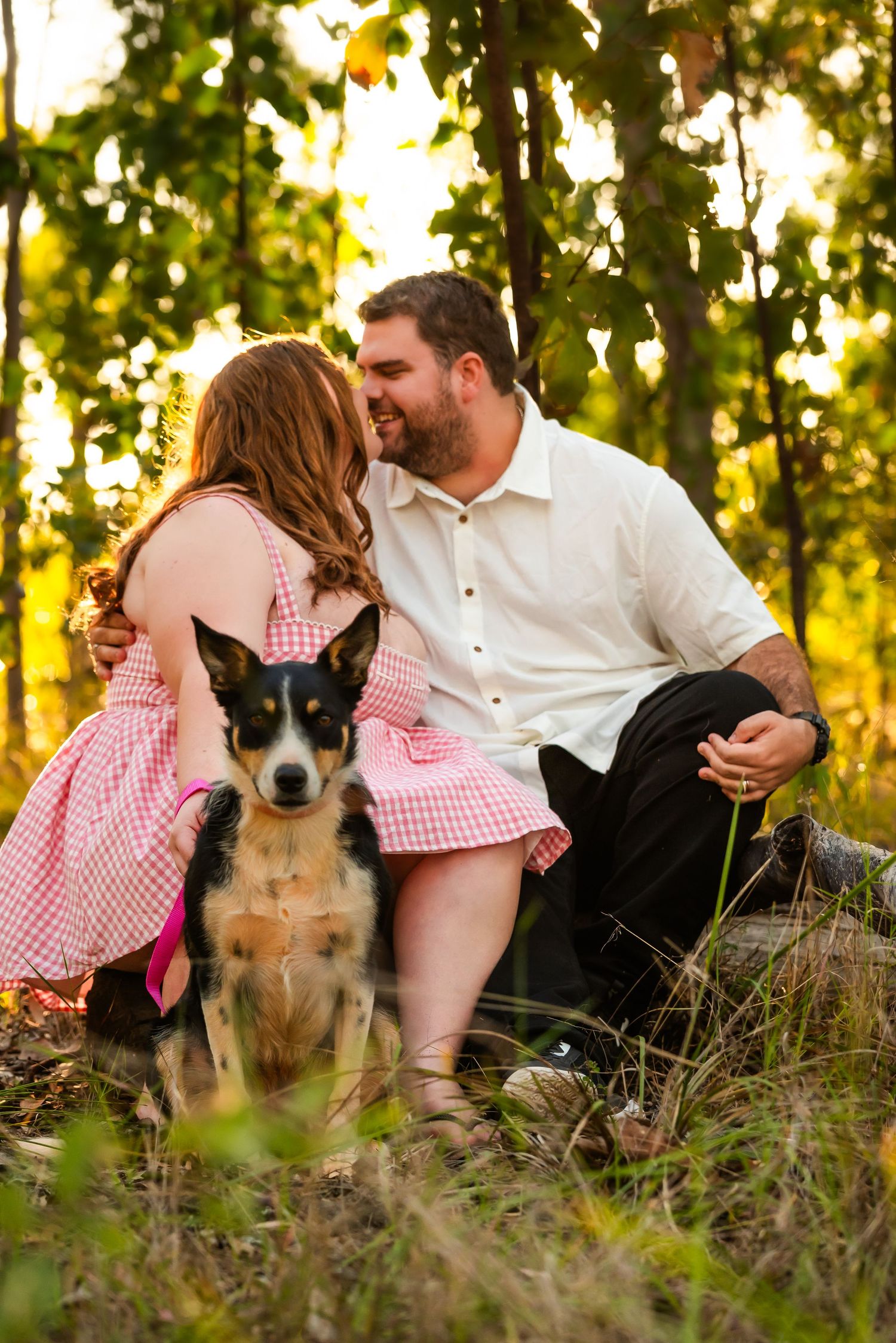 Family relaxing outdoors in a grassy field at sunset with their dog during a casual photo session.