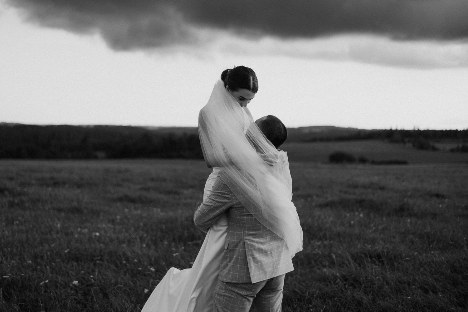 Romantic couple walking through a misty field at sunset in black and white.