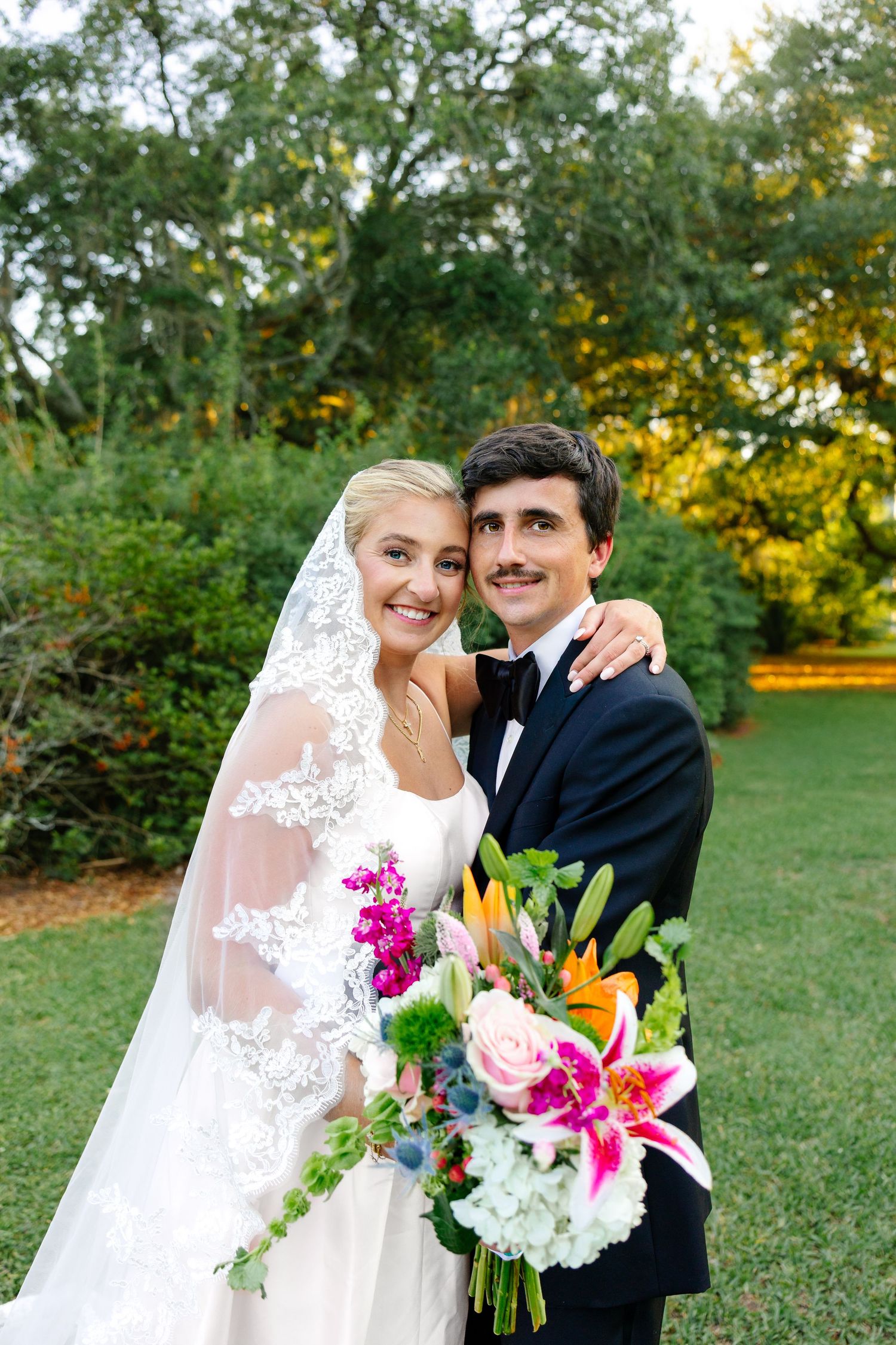 Romantic wedding couple with flowing long veil in lush garden setting.