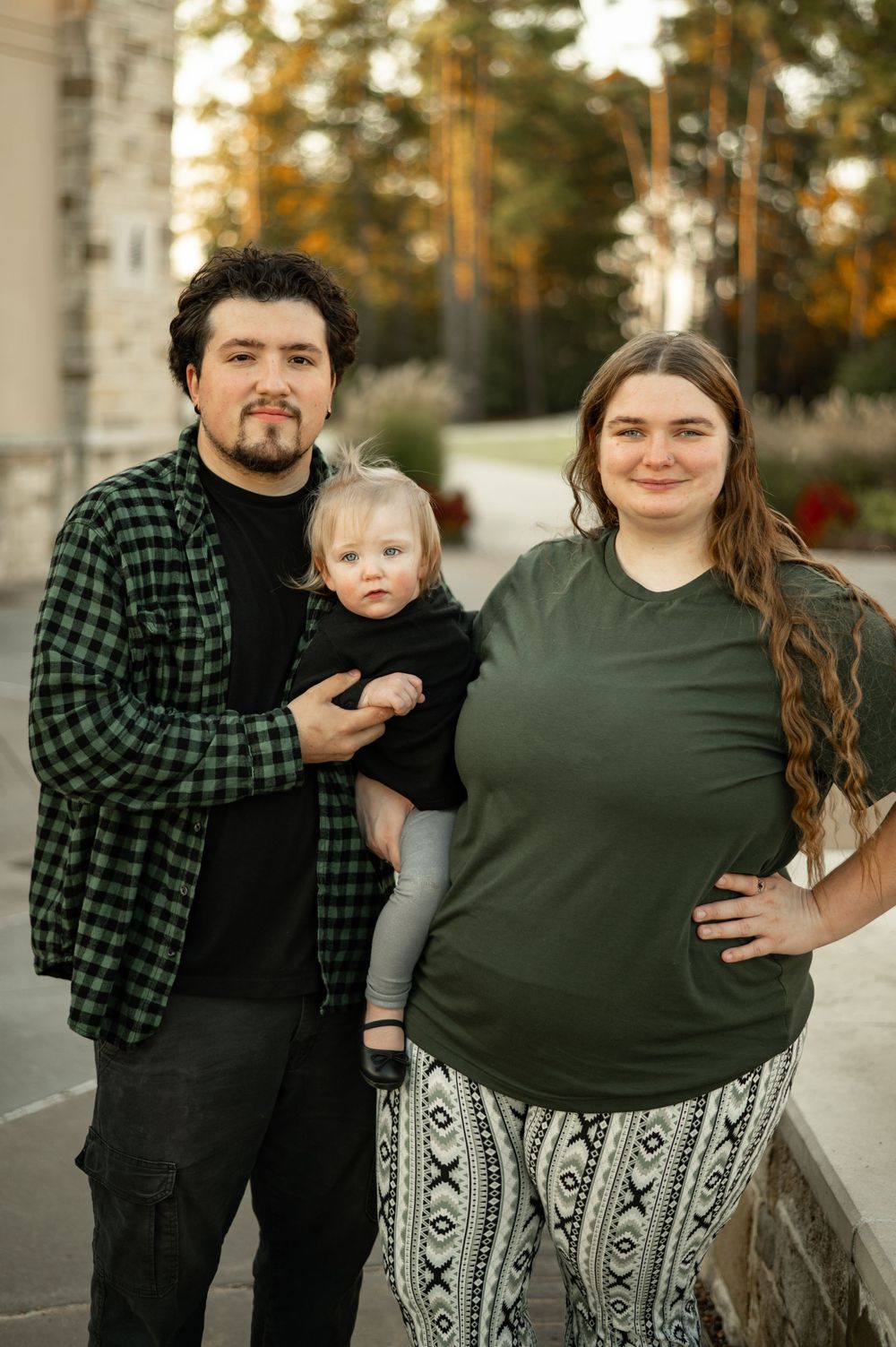 Family portrait showing a couple and child wearing coordinated outfits of green and plaid in an outdoor setting.