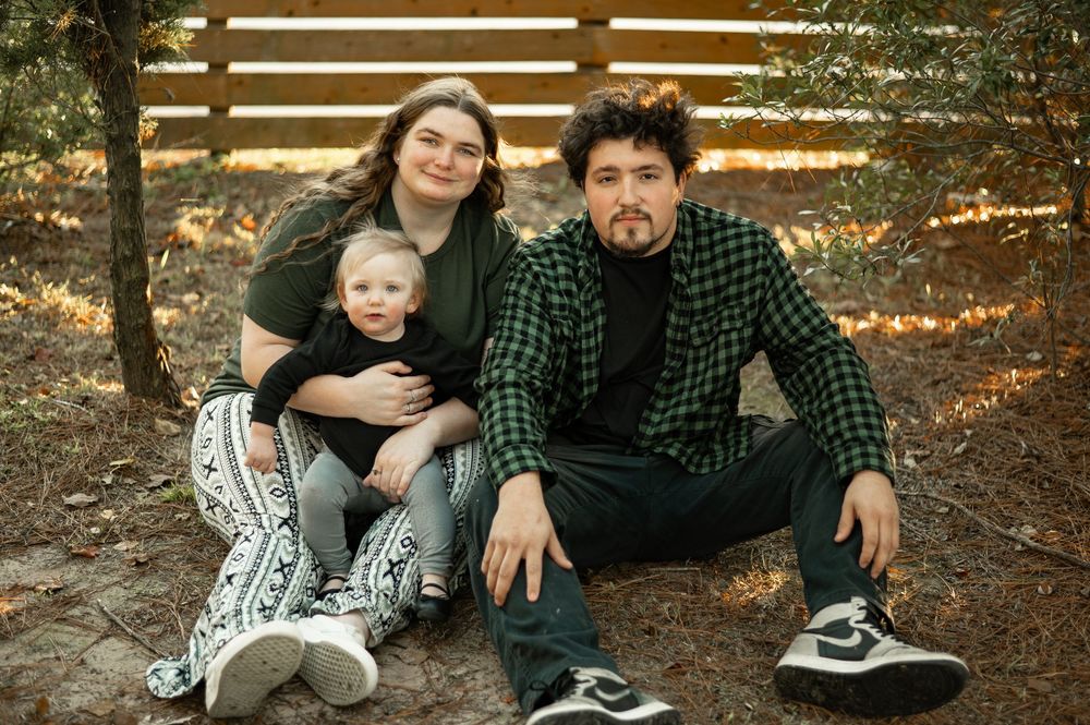 A group sits together on wooden steps in an outdoor autumn setting wearing casual clothing.