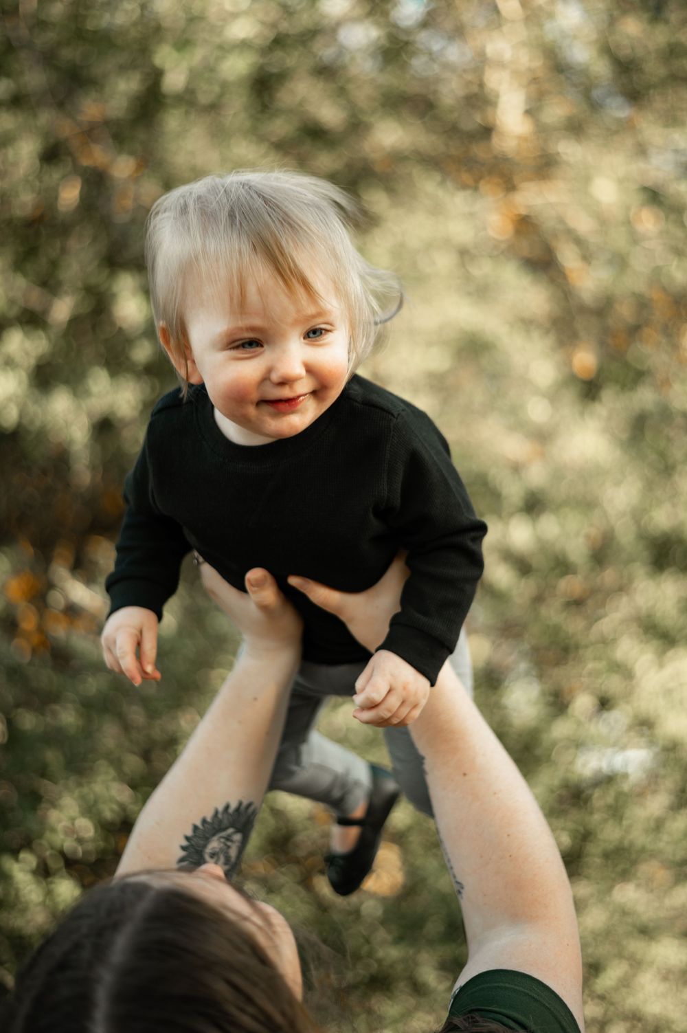 A joyful playtime moment captured outdoors with lifting motions against a soft natural background.