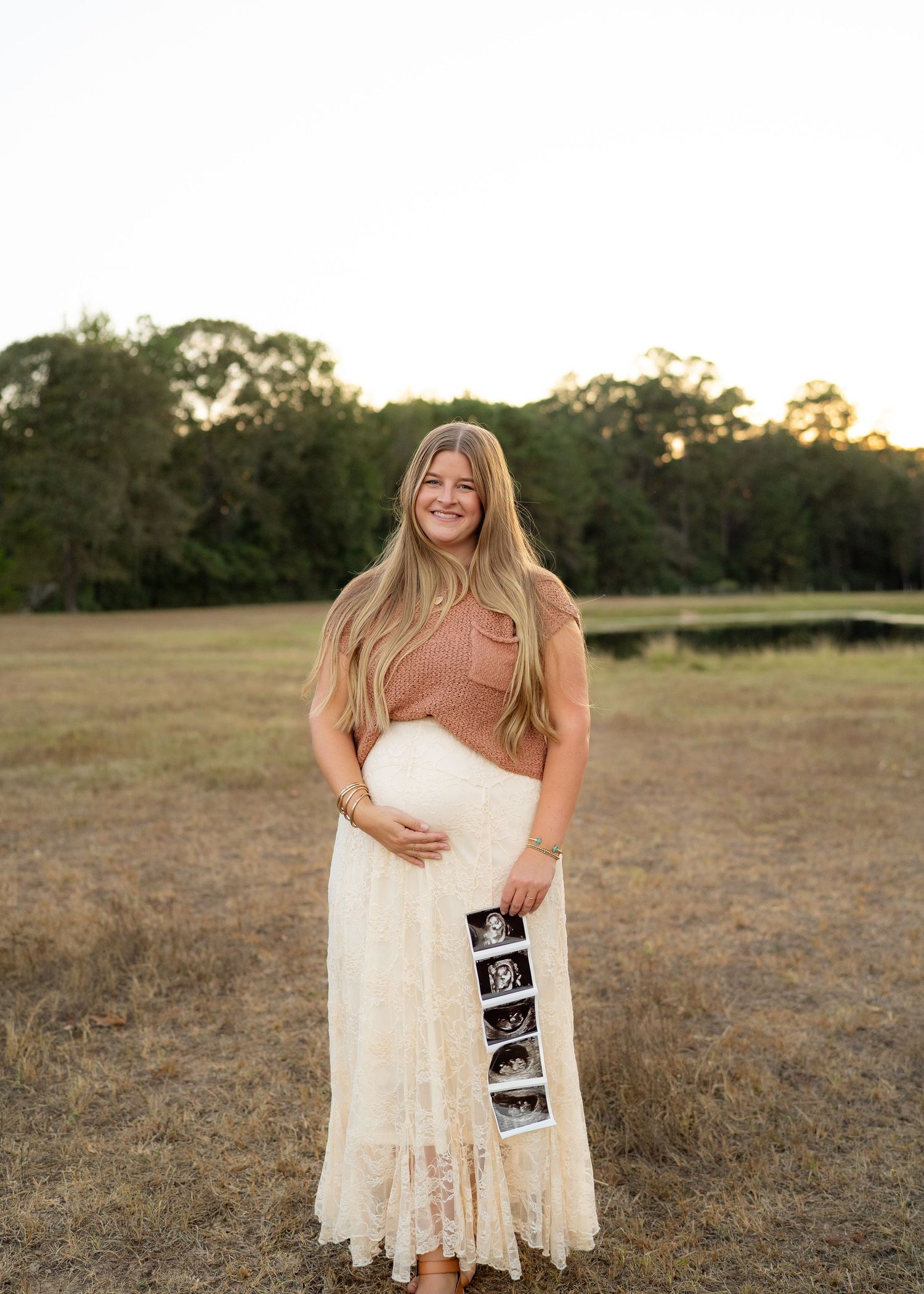 Mom smiling and holding her baby bump during an outdoor maternity photo session.