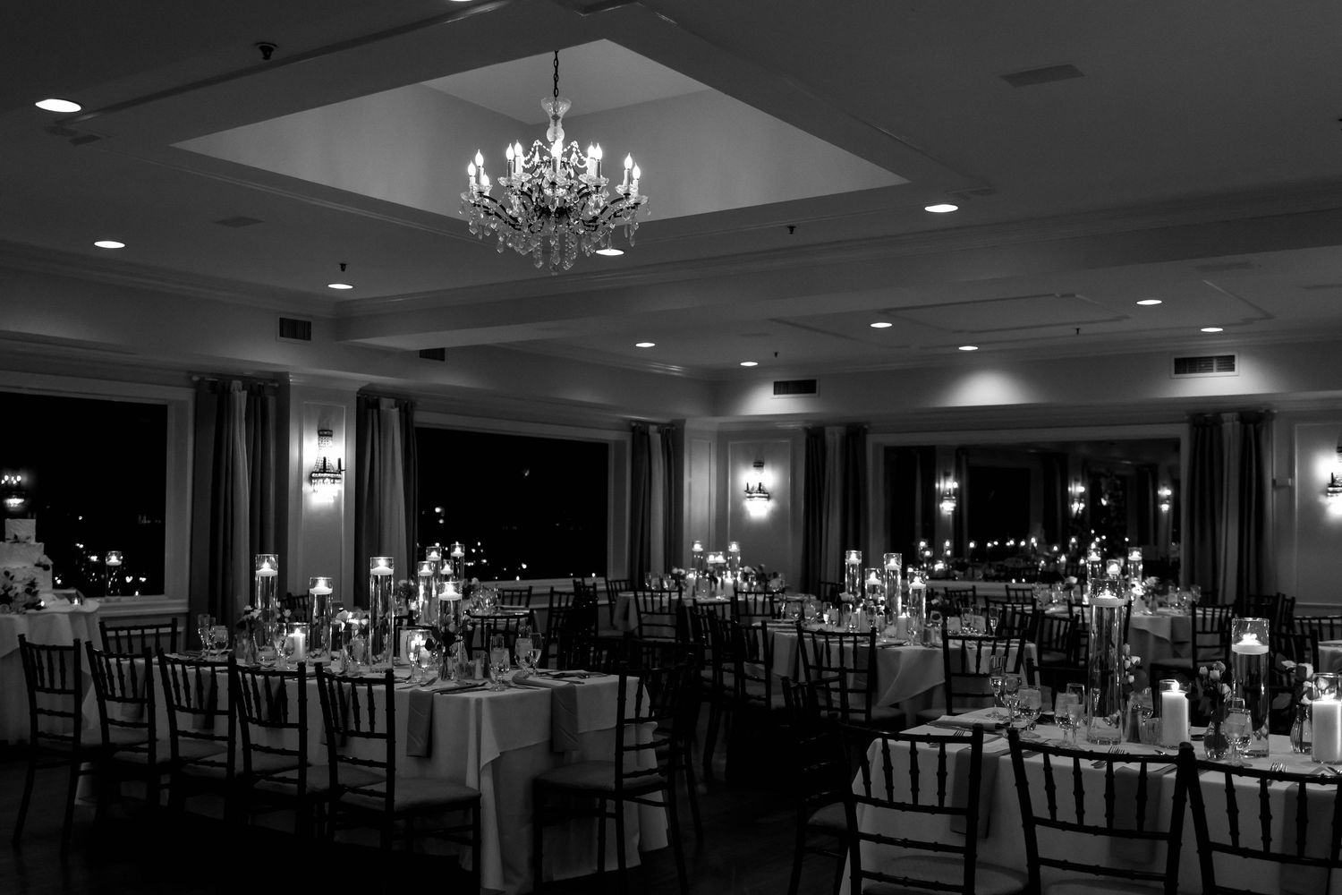 A dimly lit elegant ballroom with chandeliers and chiavari chairs arranged for a formal event.