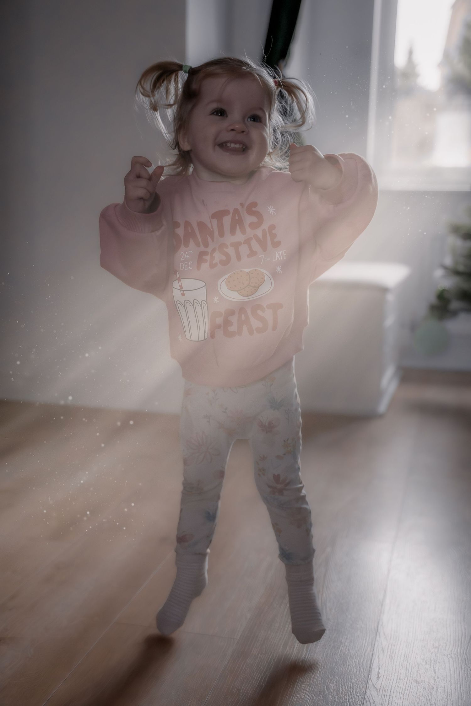 A child wearing a Santa-themed shirt dances joyfully in sunlit room creating a dreamy motion blur effect.