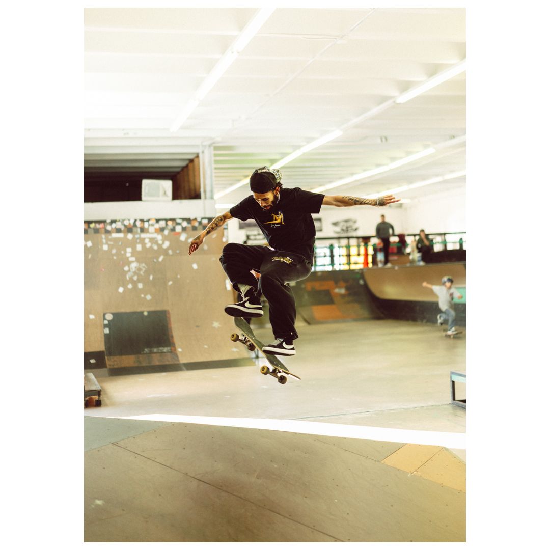 Skateboarder performing an ollie trick at an indoor skate park with ramps visible in the background.