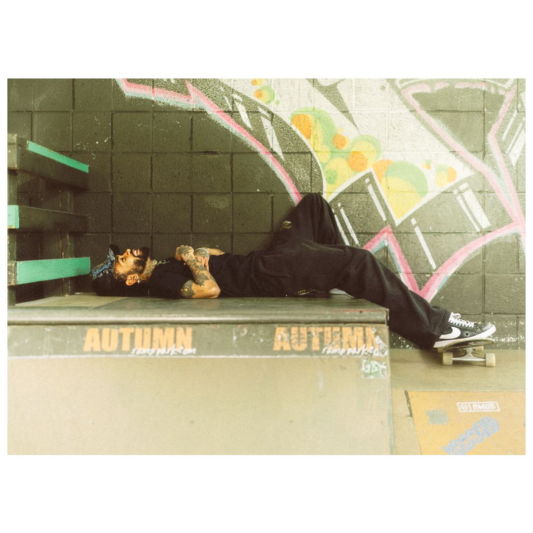 Skateboarder lying on a ramp at an outdoor skate park with colorful graffiti and Autumn branding on the wall.