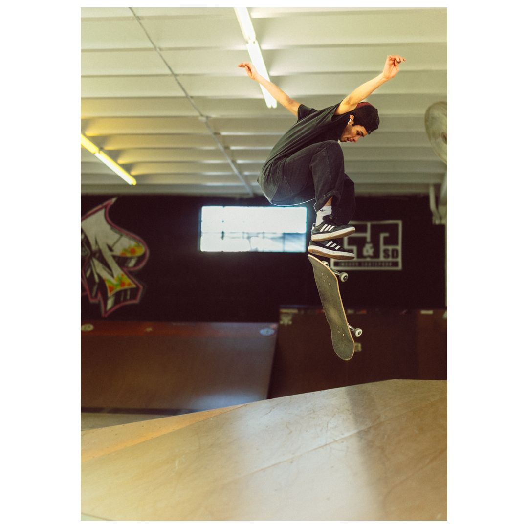 Skateboarder performing a high kickflip trick inside an indoor skate park with ramps and graffiti walls.