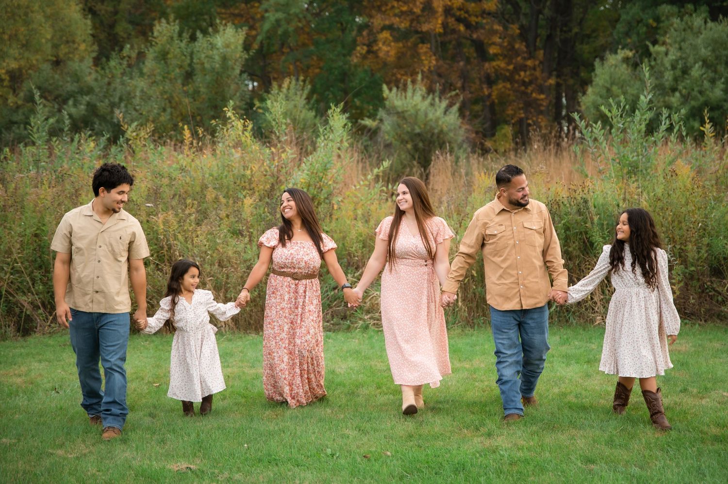 A group walks together hand in hand through a lush green outdoor setting in casual attire.