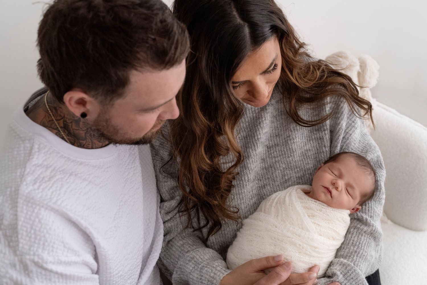 Close-up view of tiny baby wrapped in soft white blanket being cradled by loving parents.