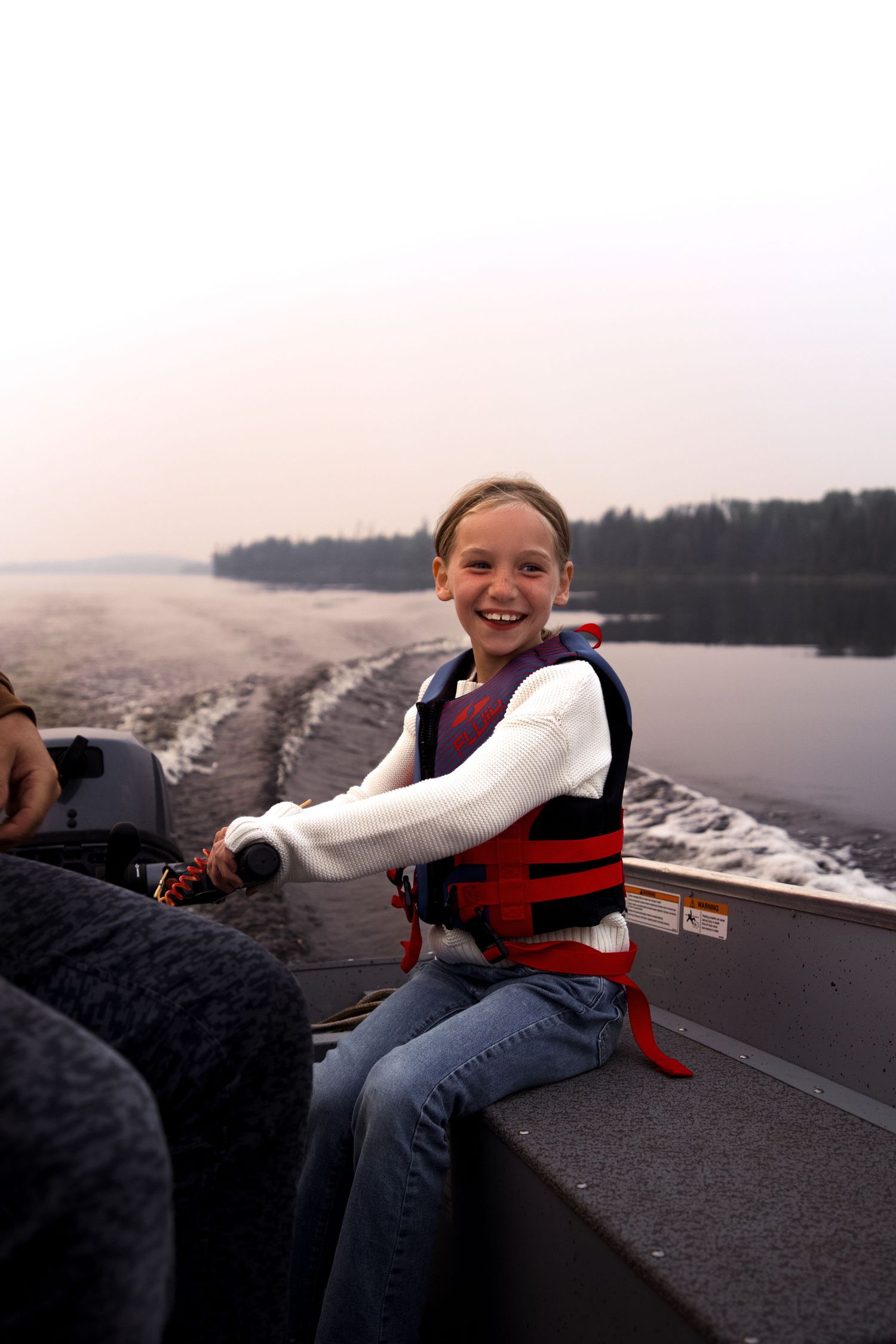 A person in a red life vest enjoys a boat ride on a lake at dusk.
