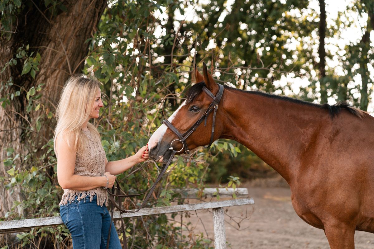 A woman in jeans pets a brown horse in a rustic outdoor setting during golden hour photoshoot with a horse in Sydney