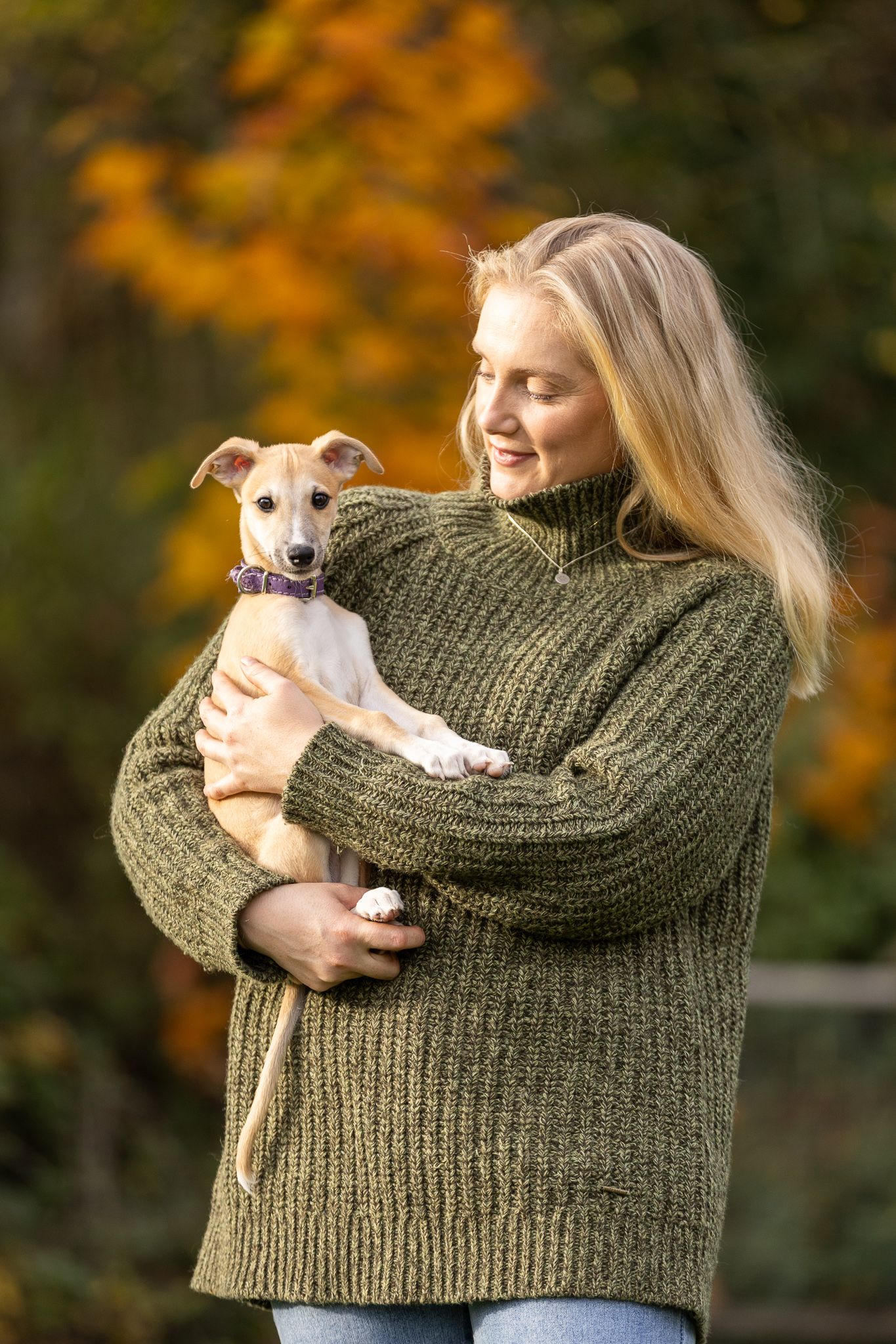 Couple sitting on elegant wooden staircase with green carpet with their brown rescue dog in cozy home setting.