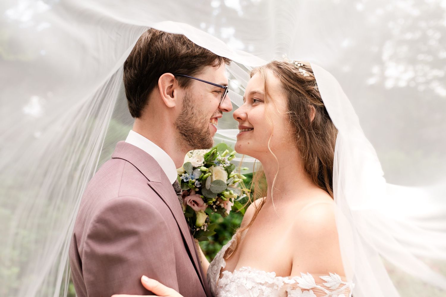 Lachende bruid en bruidegom lachen tijdens fotoshoot onder sluier, gefotografeerd door christelijke trouwfotograaf Amersfoort