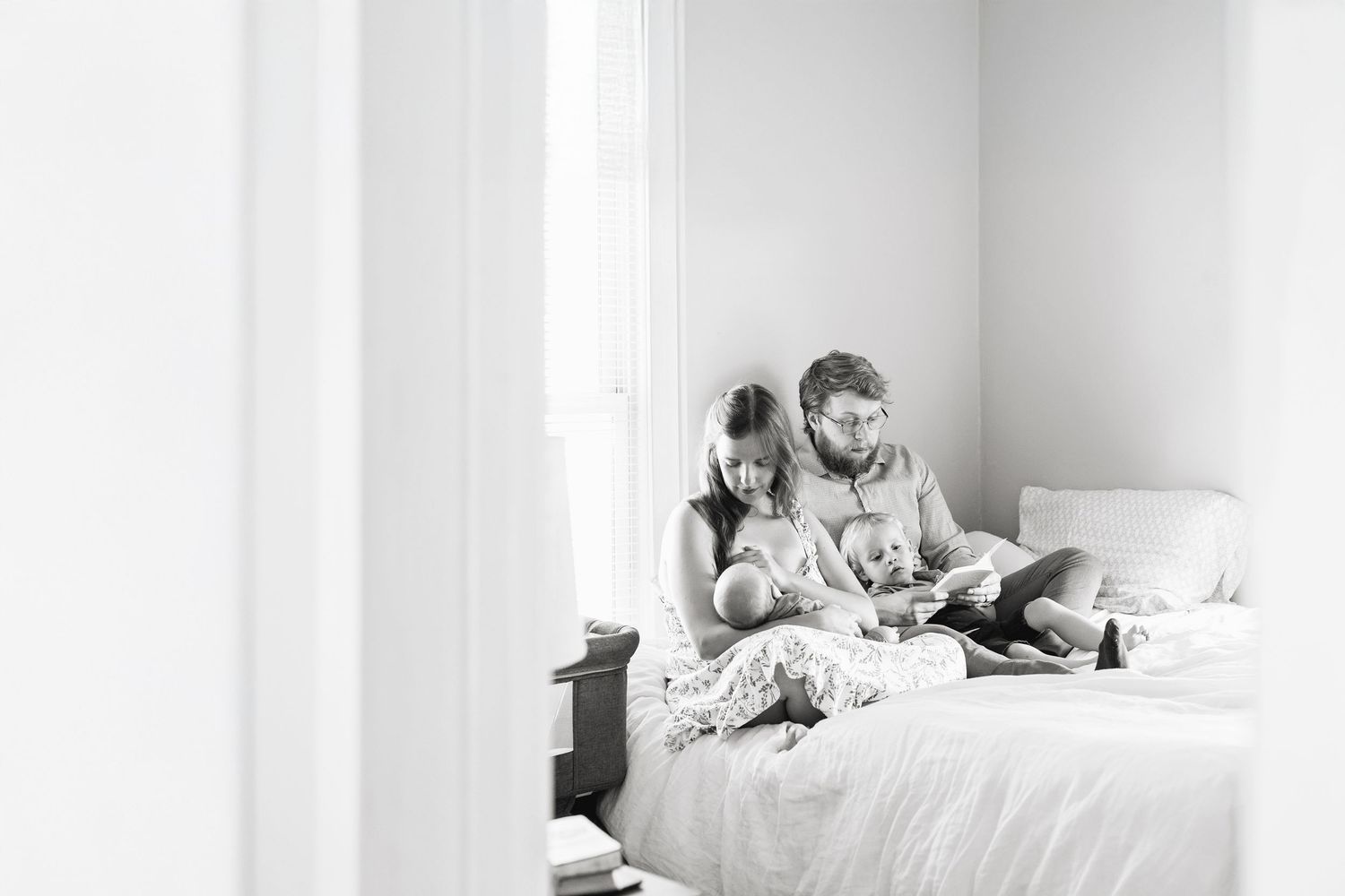 A couple sits together on a white bed reading books in a minimalist black and white setting during in-home photoshoot in Mason City, Iowa.