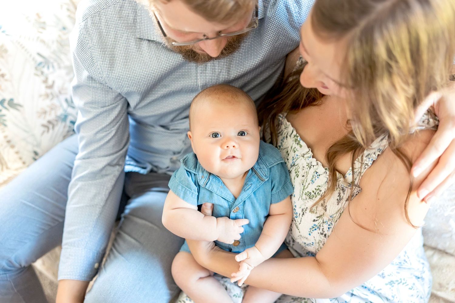 A family cuddling together while sitting on a couch in a sunlit room during milestone family session at their hone in Garner Iowa.