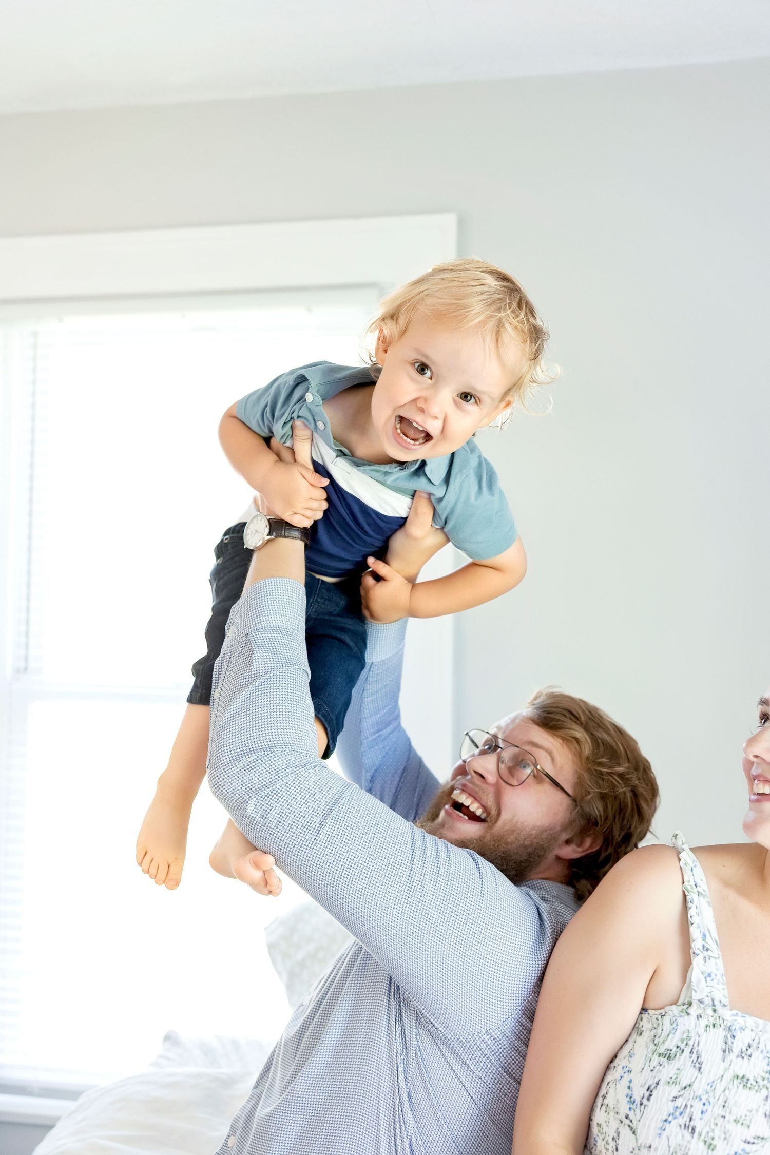 A playful moment captured as a parent lifts a small child in the air while playing together in a bright room.