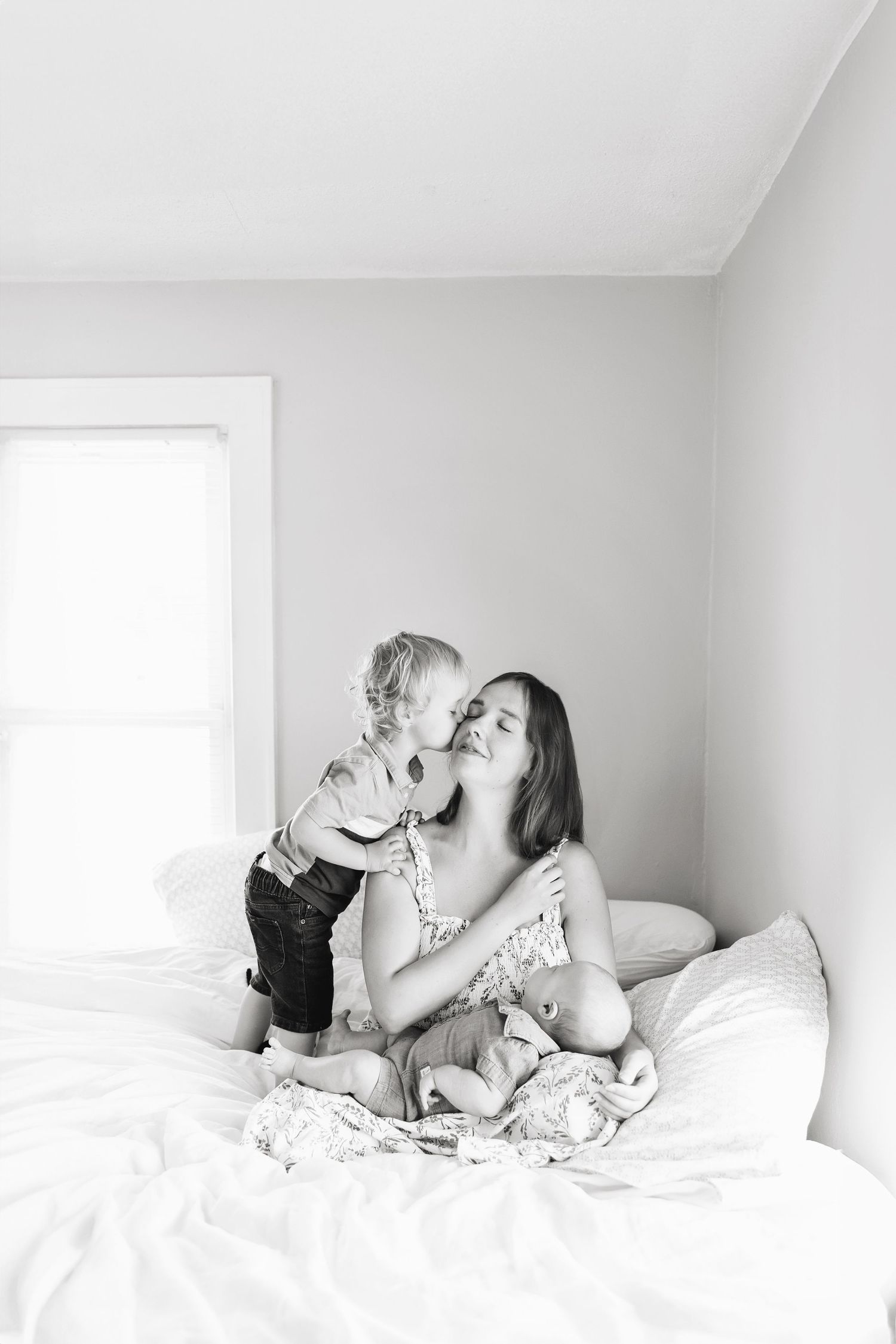 A candid black and white photo shows a family relaxing together on white bedding in a minimalist setting in Clear Lake home.