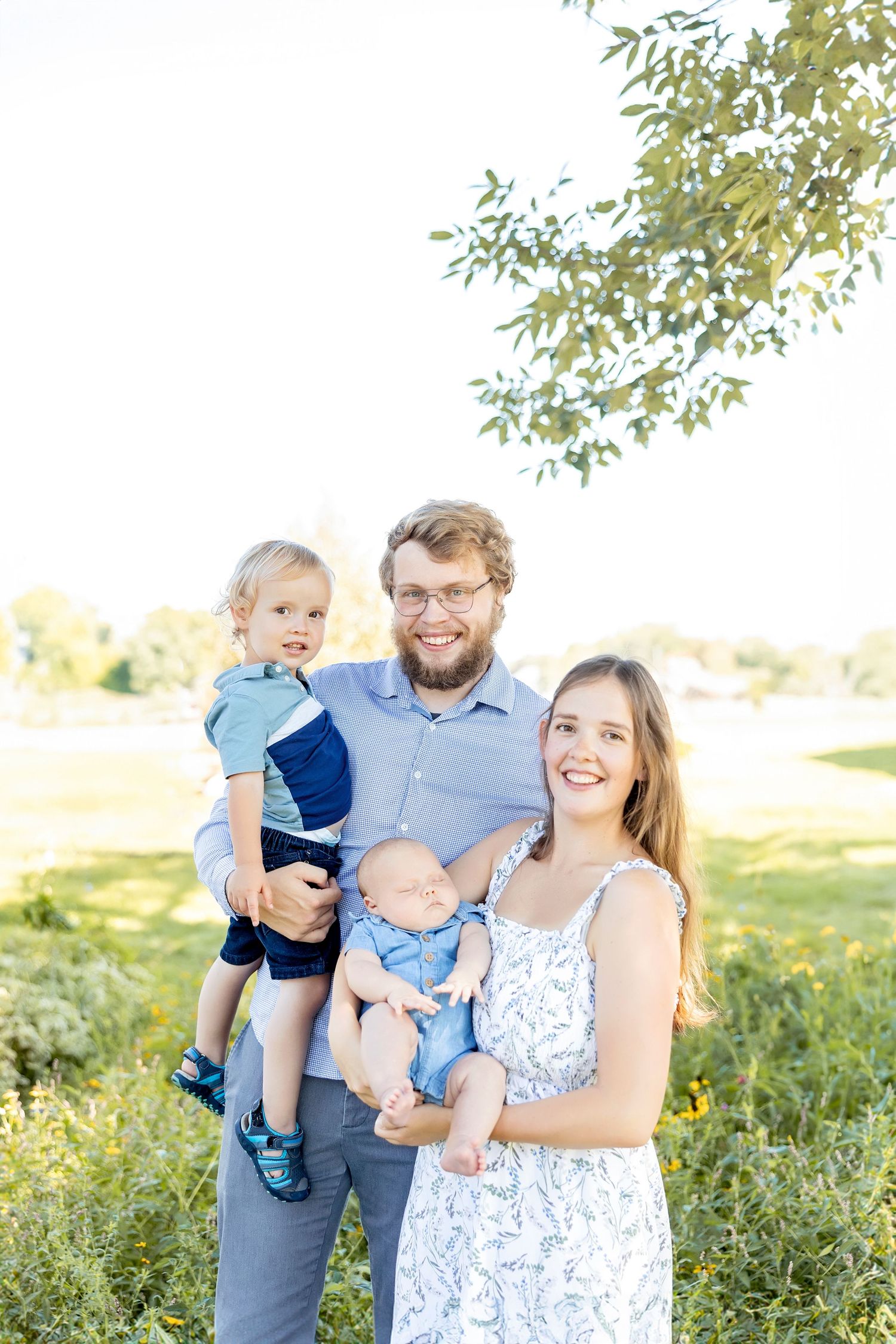 Family enjoying a sunny day outdoors in a grassy field with trees in the background.
