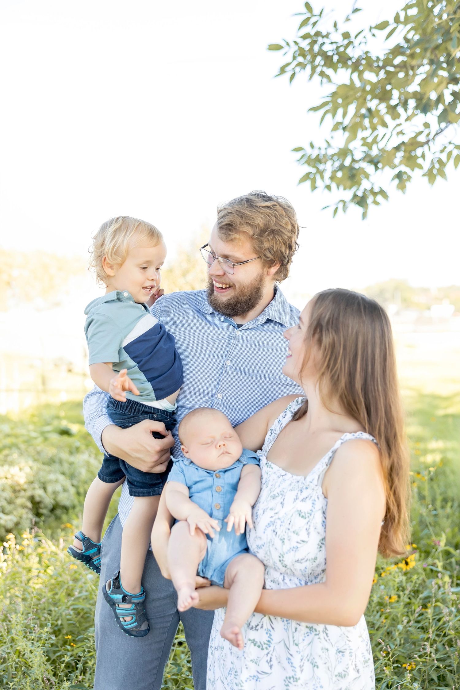 Family enjoying a tender outdoor moment together in a sunlit field with wildflowers.