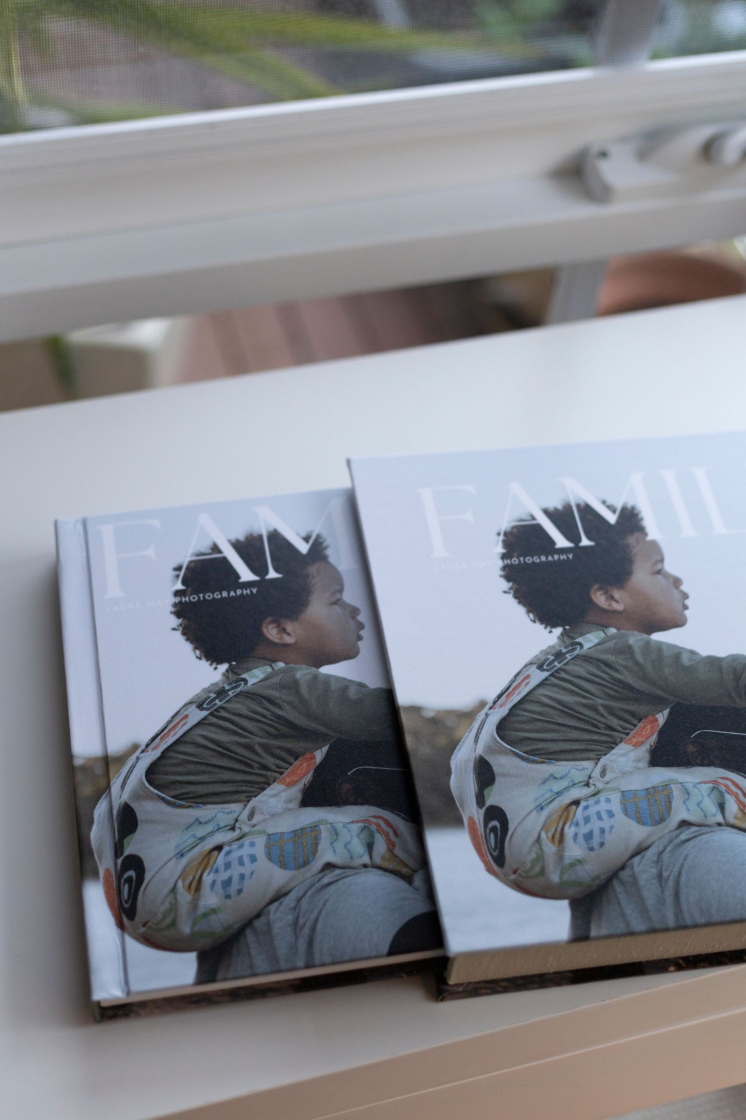 Two identical hardcover books on a windowsill showing a profile view of a person in a patterned jacket.