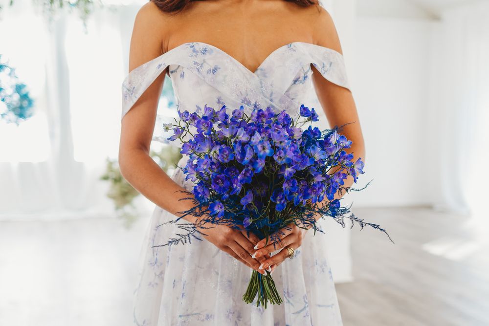 Bride holding vibrant blue delphinium bouquet against white background.