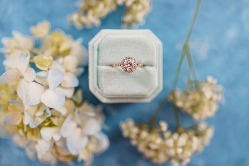 Rose gold engagement ring in mint green velvet box with delicate white flowers.