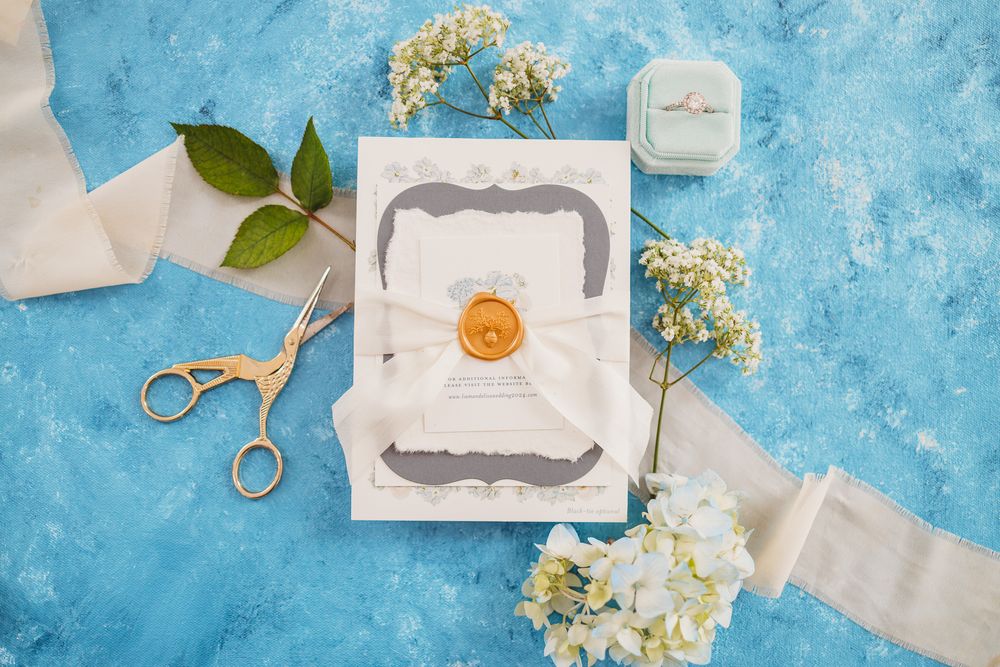 Flat lay of wedding stationery and delicate flowers on bright blue background.