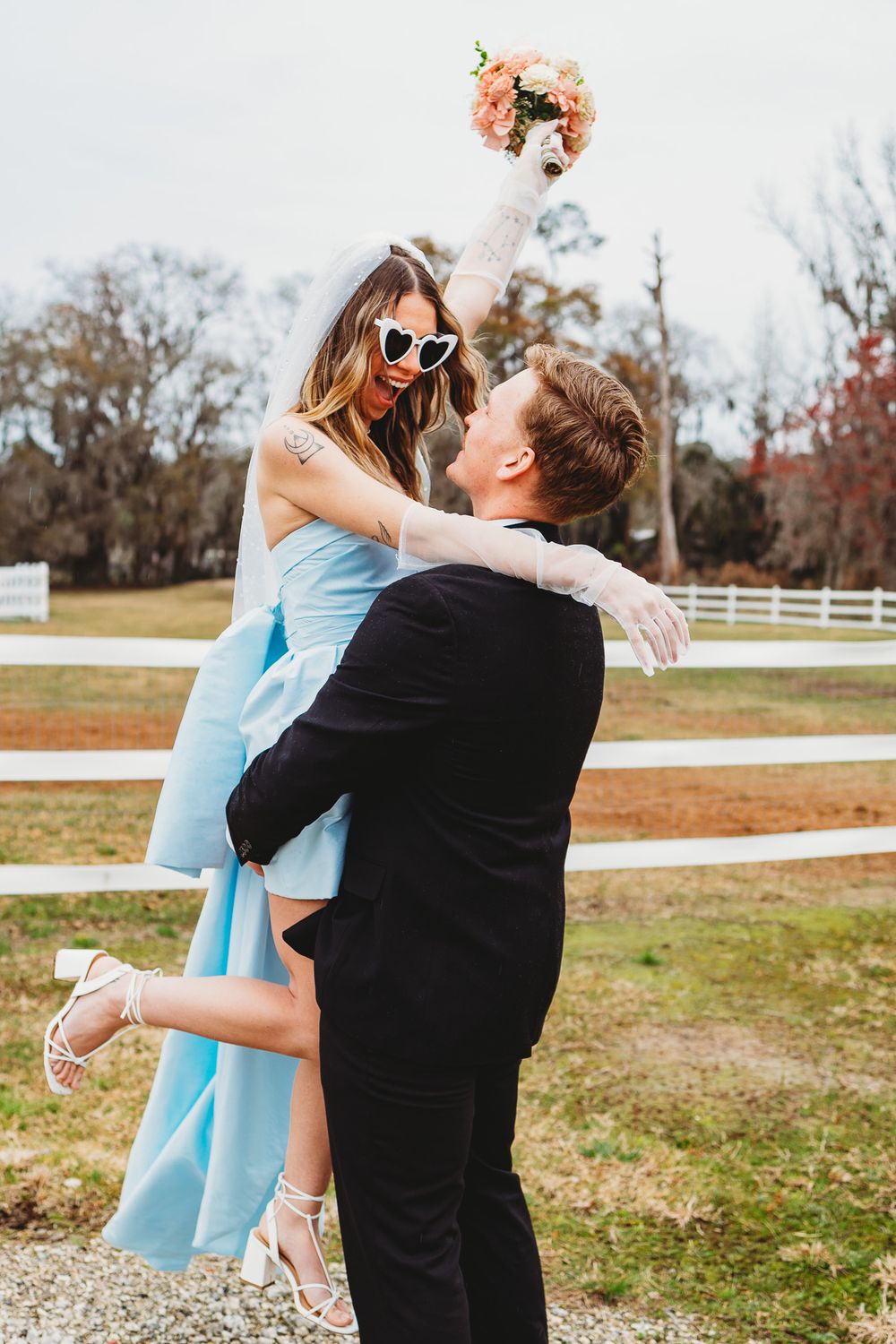 Playful couple in formal attire sharing a joyful moment outdoors with bouquet toss.