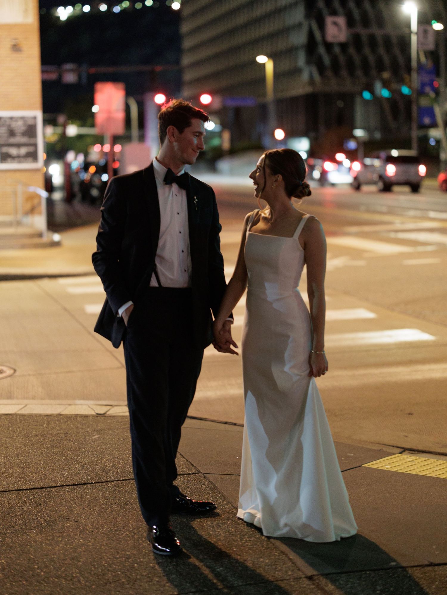 A couple in formal wedding attire shares an intimate moment on a city street at night.