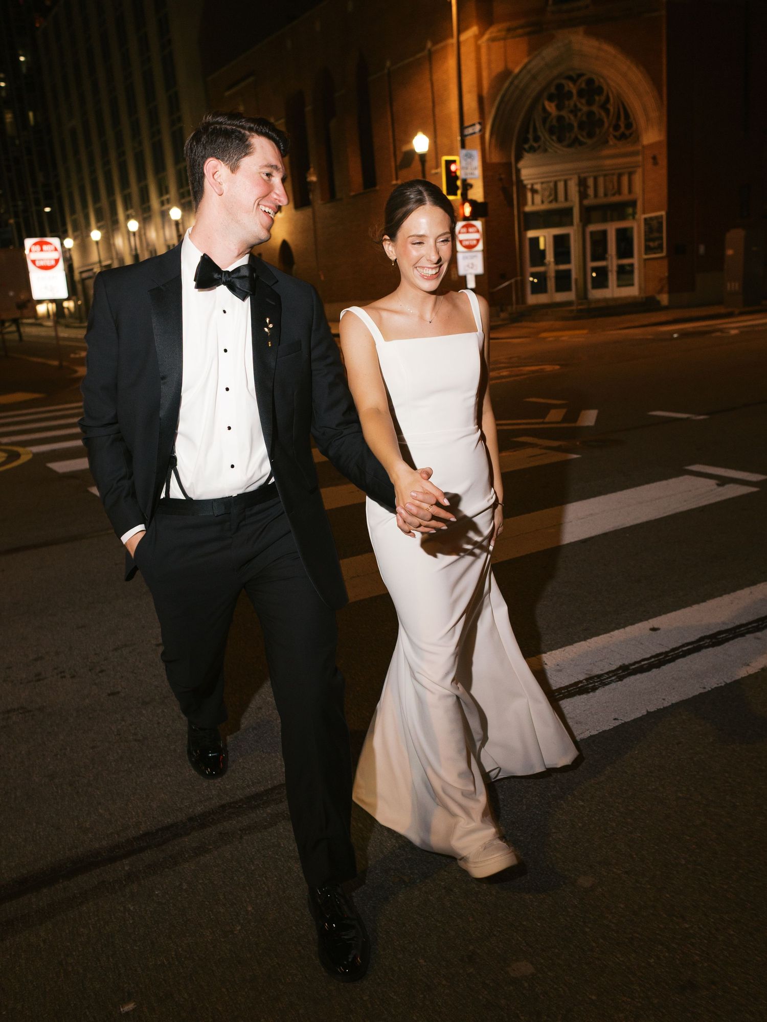 A couple walks together at night along a city street after their wedding celebration.