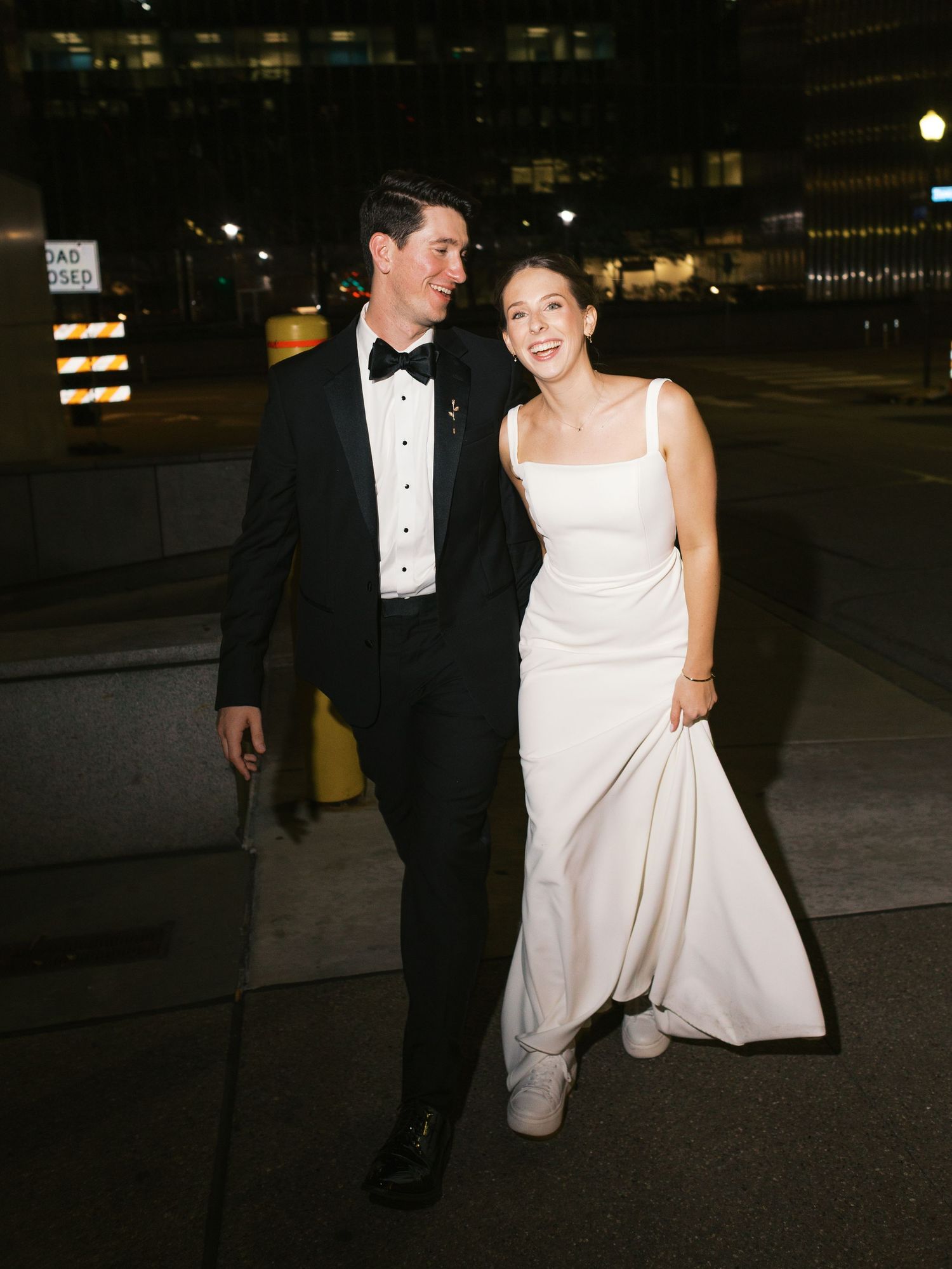A couple walking together at night, with the person in a tuxedo and their partner in an elegant white wedding dress.