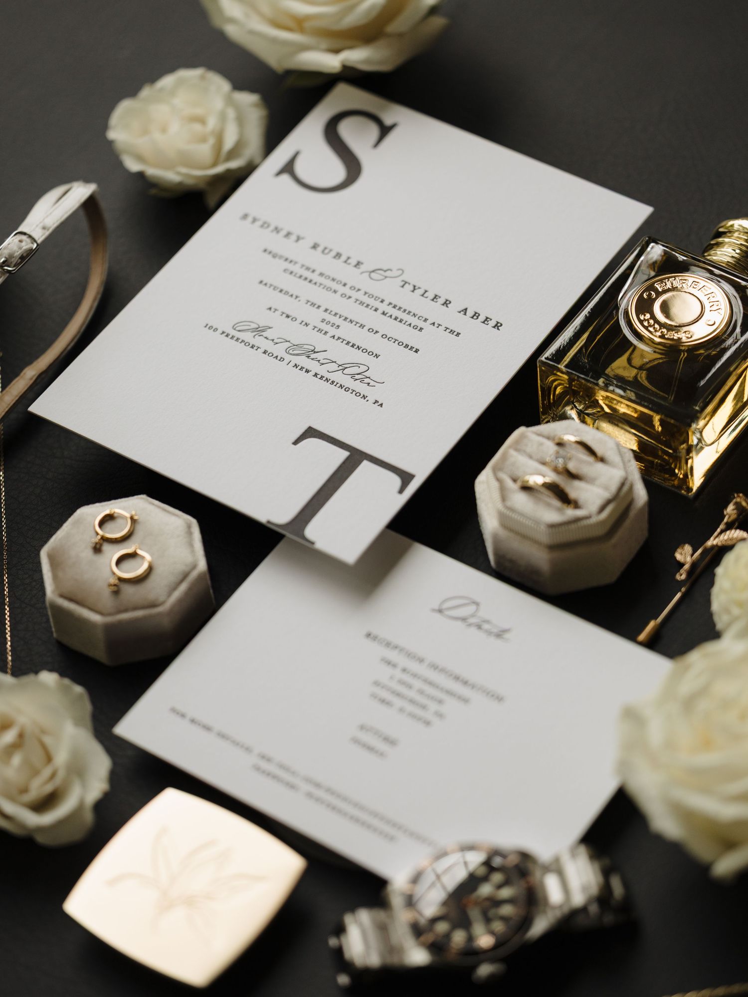 Elegant wedding stationery with white roses and gold accents displayed on dark background.