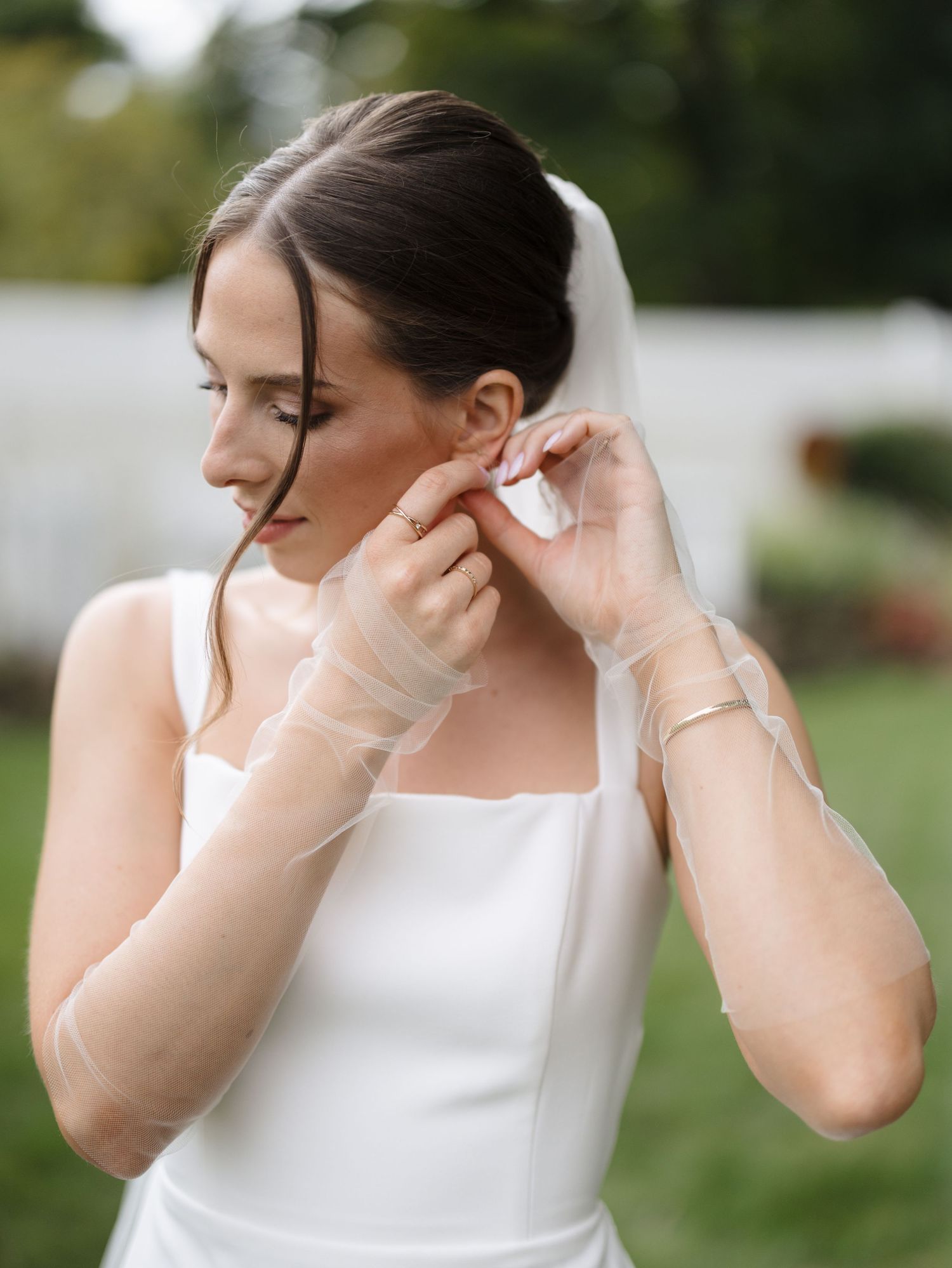 A sequence of photos showing someone putting on delicate pearl earrings outdoors in a white dress.