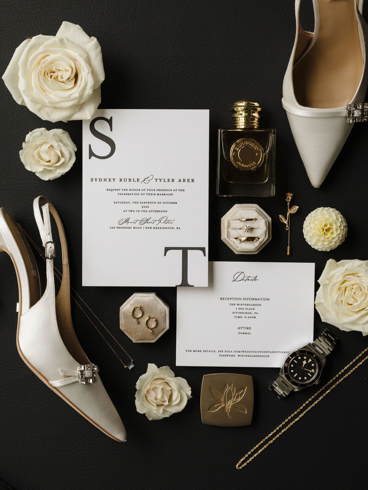 Elegant wedding details flatlay with white roses, invitations, jewelry, and white heels on black background.