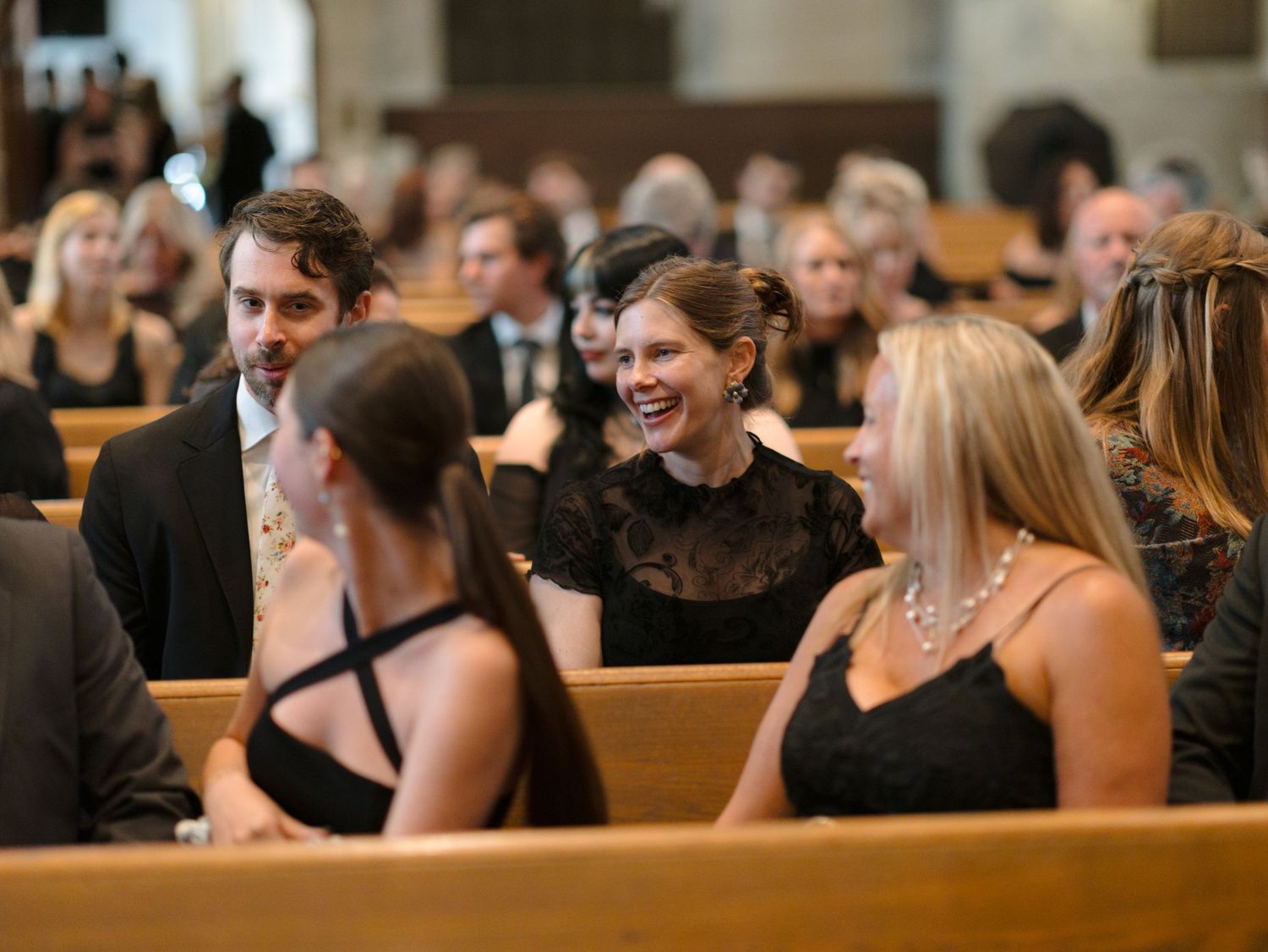 Wedding guests seated in church pews during a ceremony with natural lighting.
