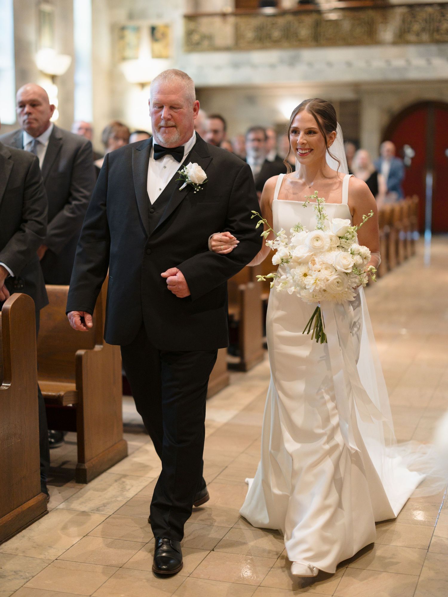 Wedding ceremony processional showing bride and father walking down church aisle in elegant formal attire.