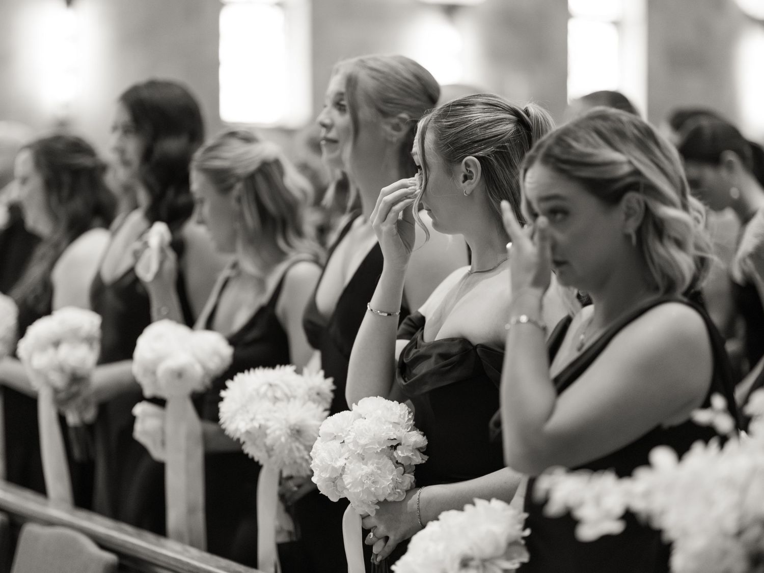 Wedding guests seated in rows watch emotional ceremony with white floral bouquets visible.