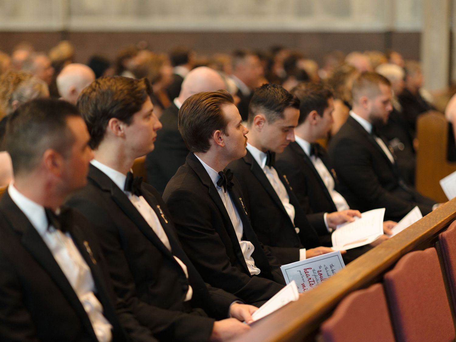 Wedding guests seated in formal attire watching ceremony in ornate church sanctuary.