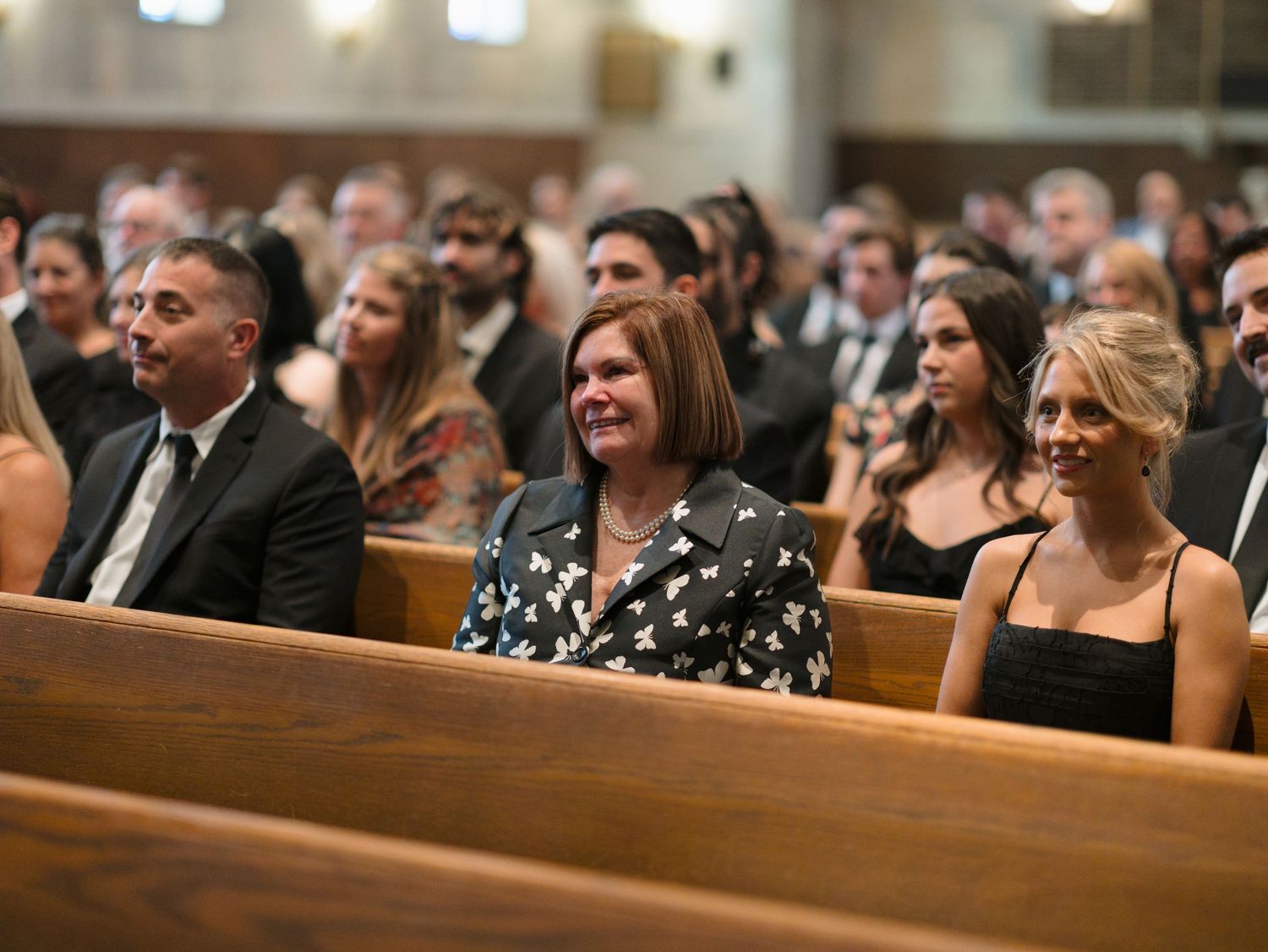 Wedding guests seated in church pews smile and react during a ceremony.