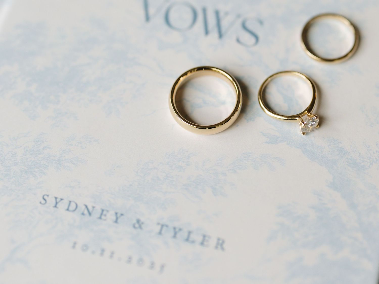 Wedding rings and vows book photographed on a light blue textured surface with delicate details.
