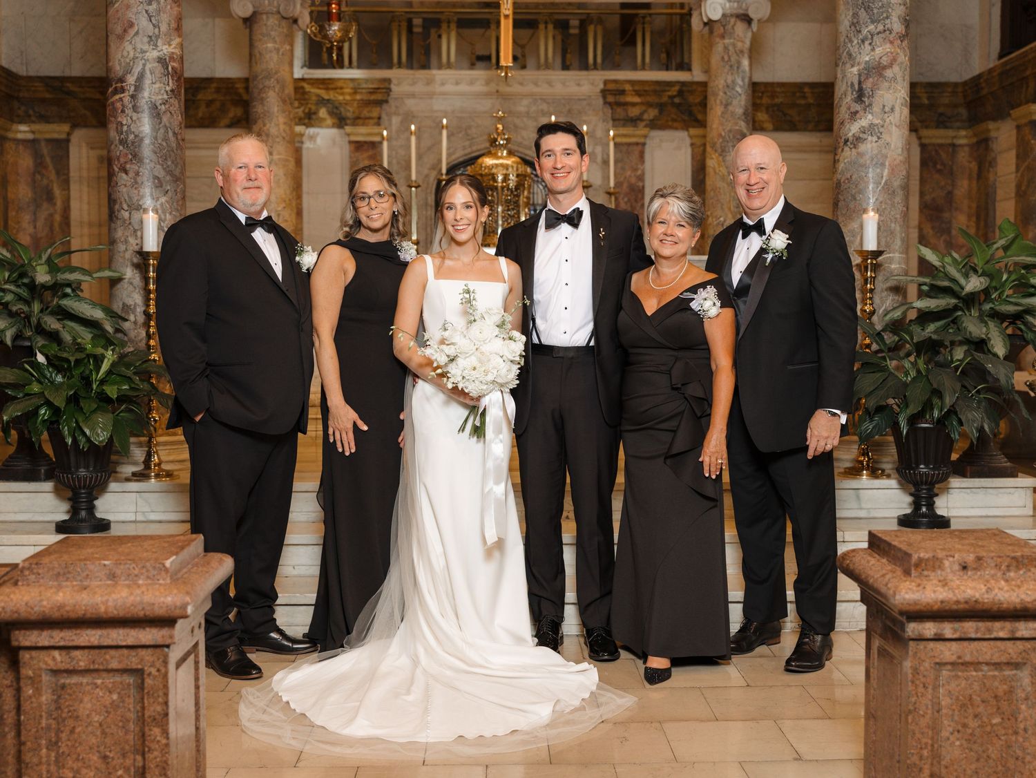 A formal wedding party poses together in an elegant church setting with marble columns.