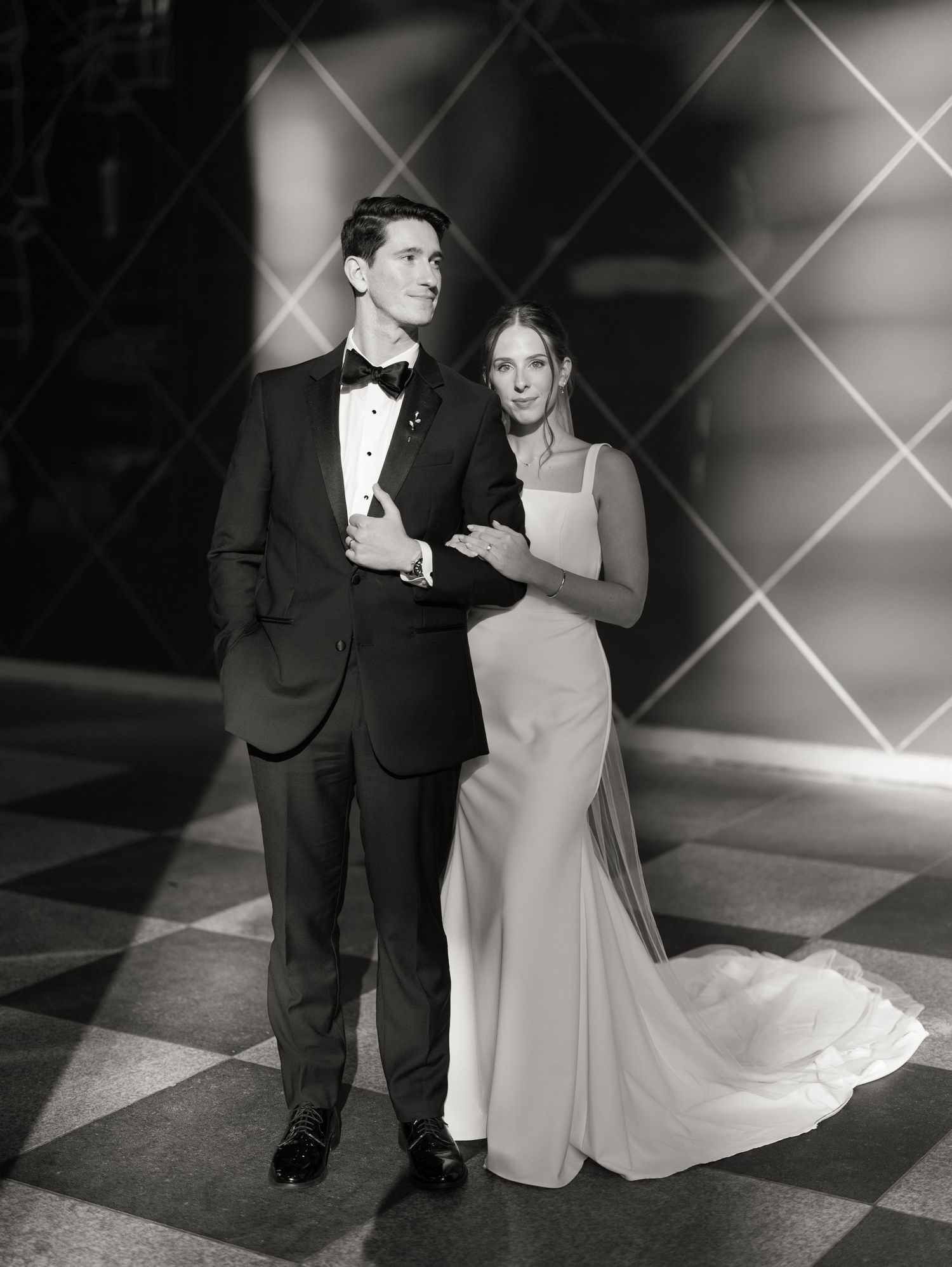 A black and white wedding photo of a couple dancing on a checkered floor.
