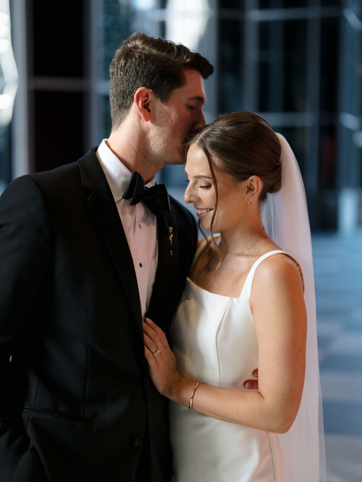A romantic moment between newlyweds in formal attire against a modern backdrop.