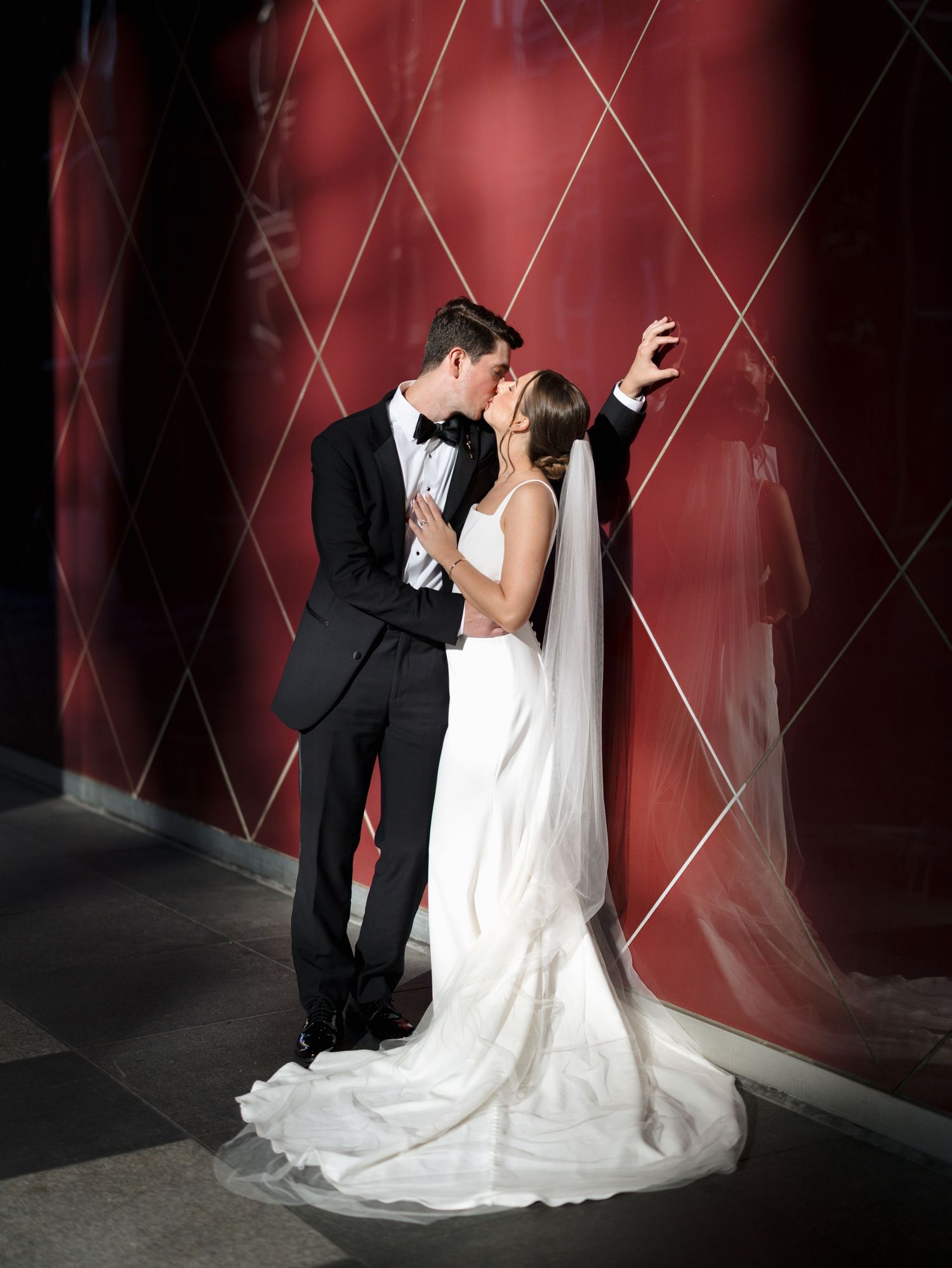 A romantic wedding portrait against a deep red wall with dramatic lighting and shadows.