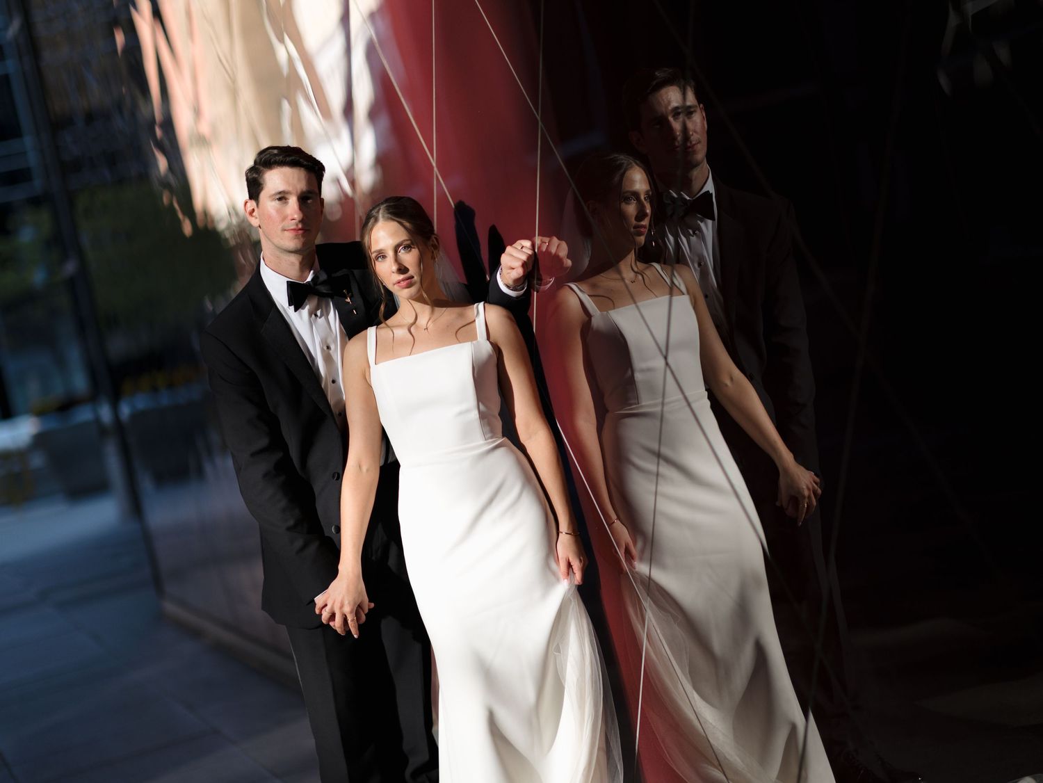 Wedding party members in formal attire walk through dimly lit venue space.