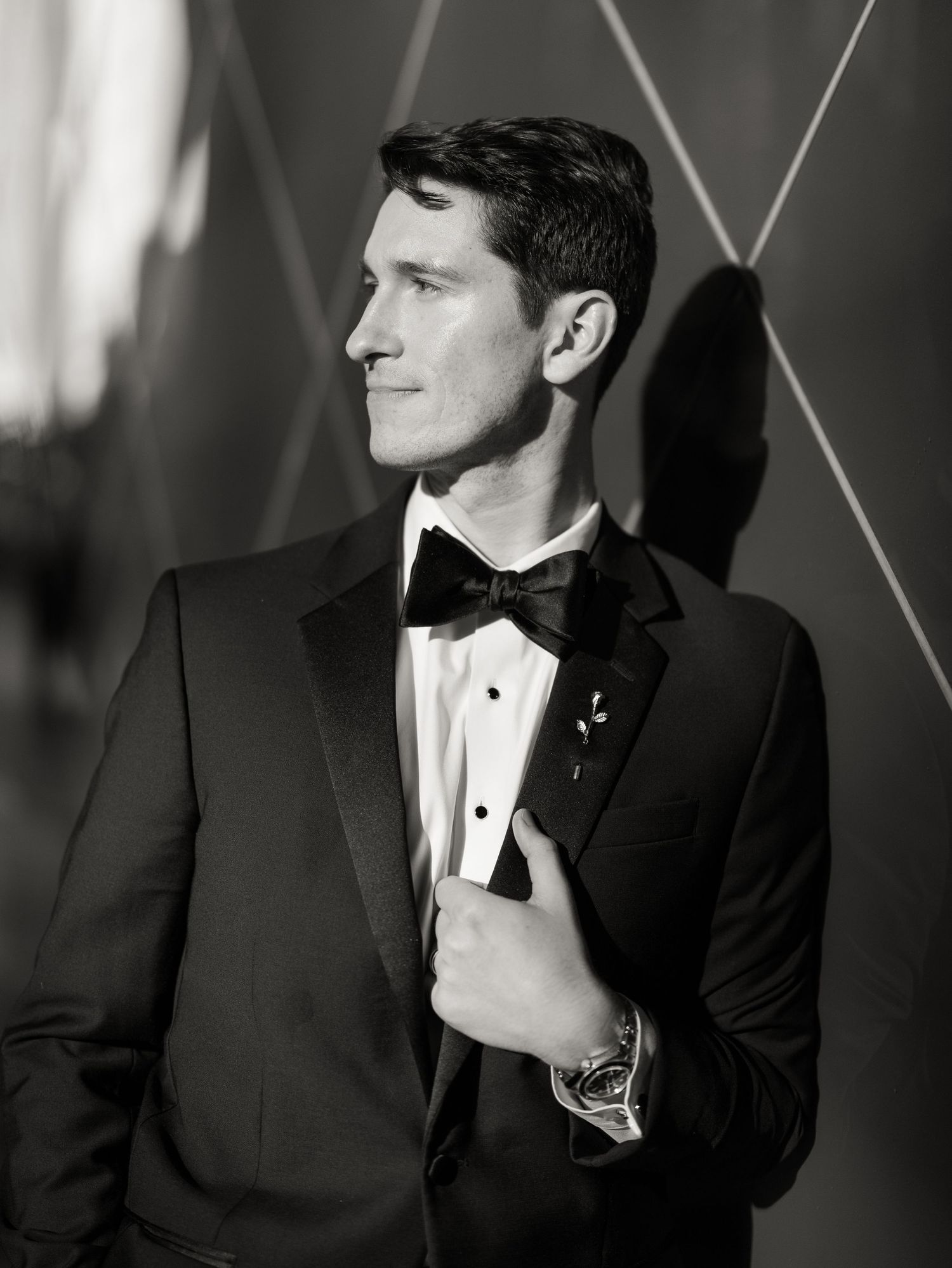 A black and white portrait of a groom in a tuxedo with dramatic lighting.