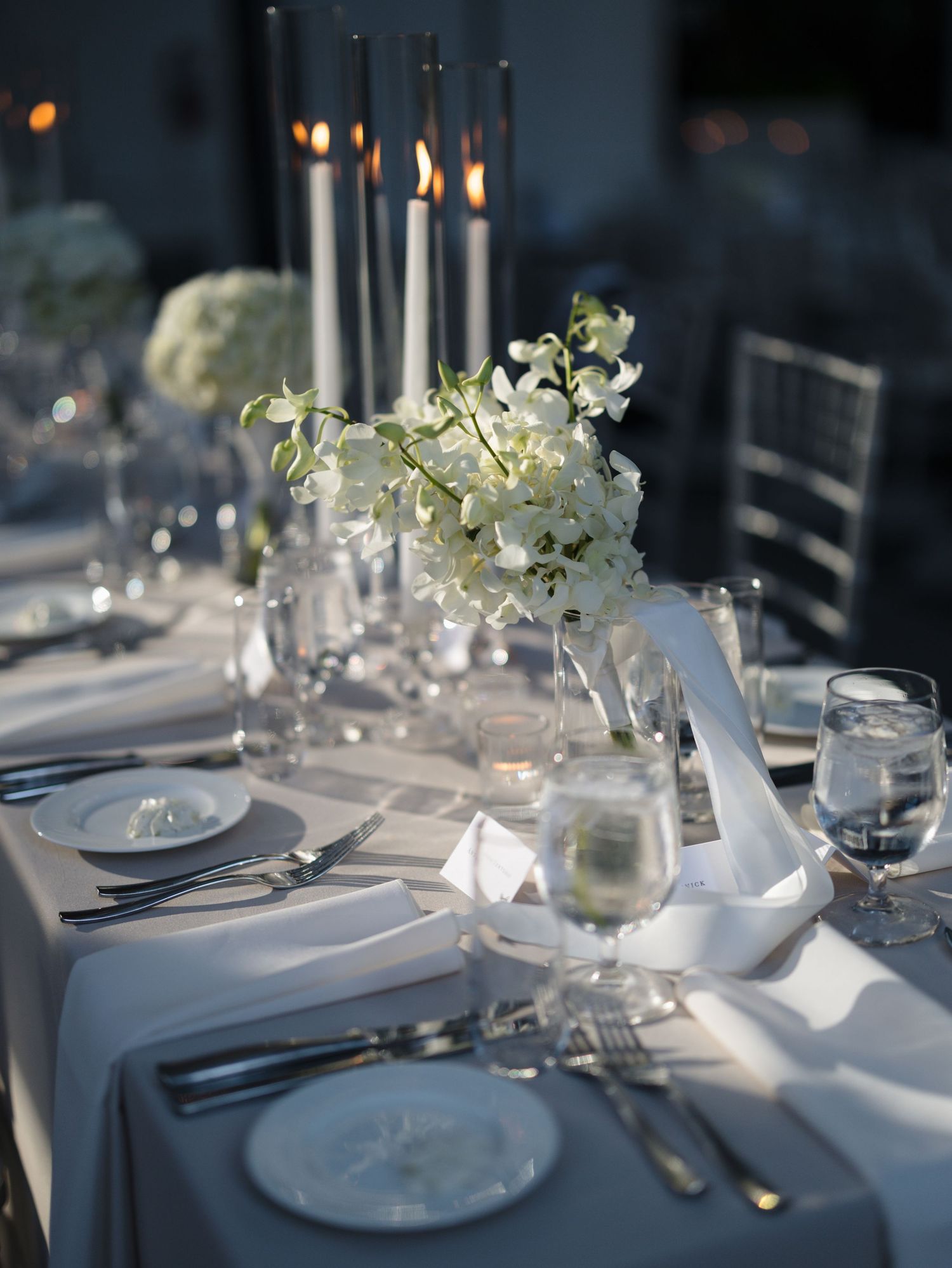 Elegant wedding reception table settings with white floral centerpieces and formal place settings.