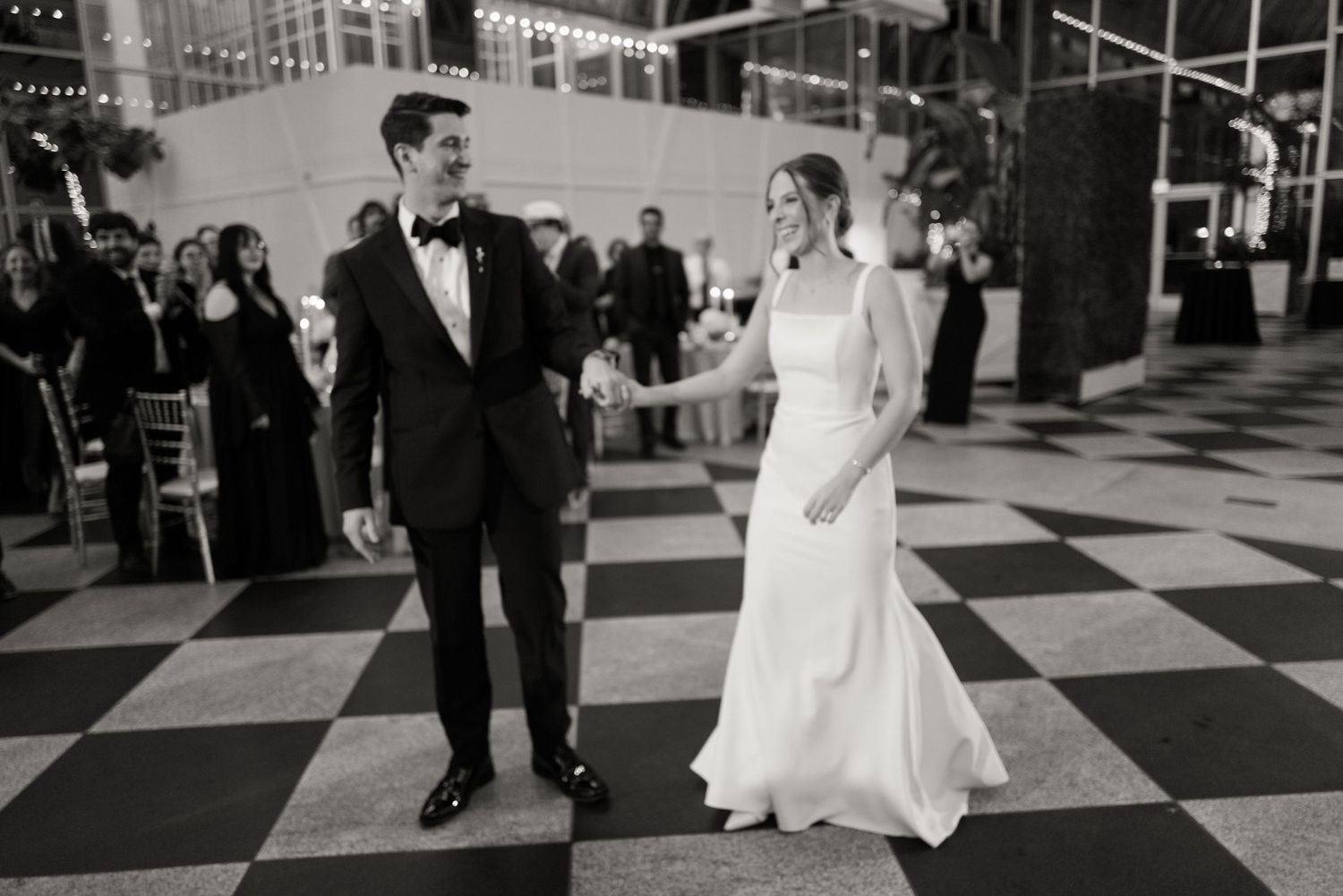A couple in wedding attire walks across a black and white checkered floor.