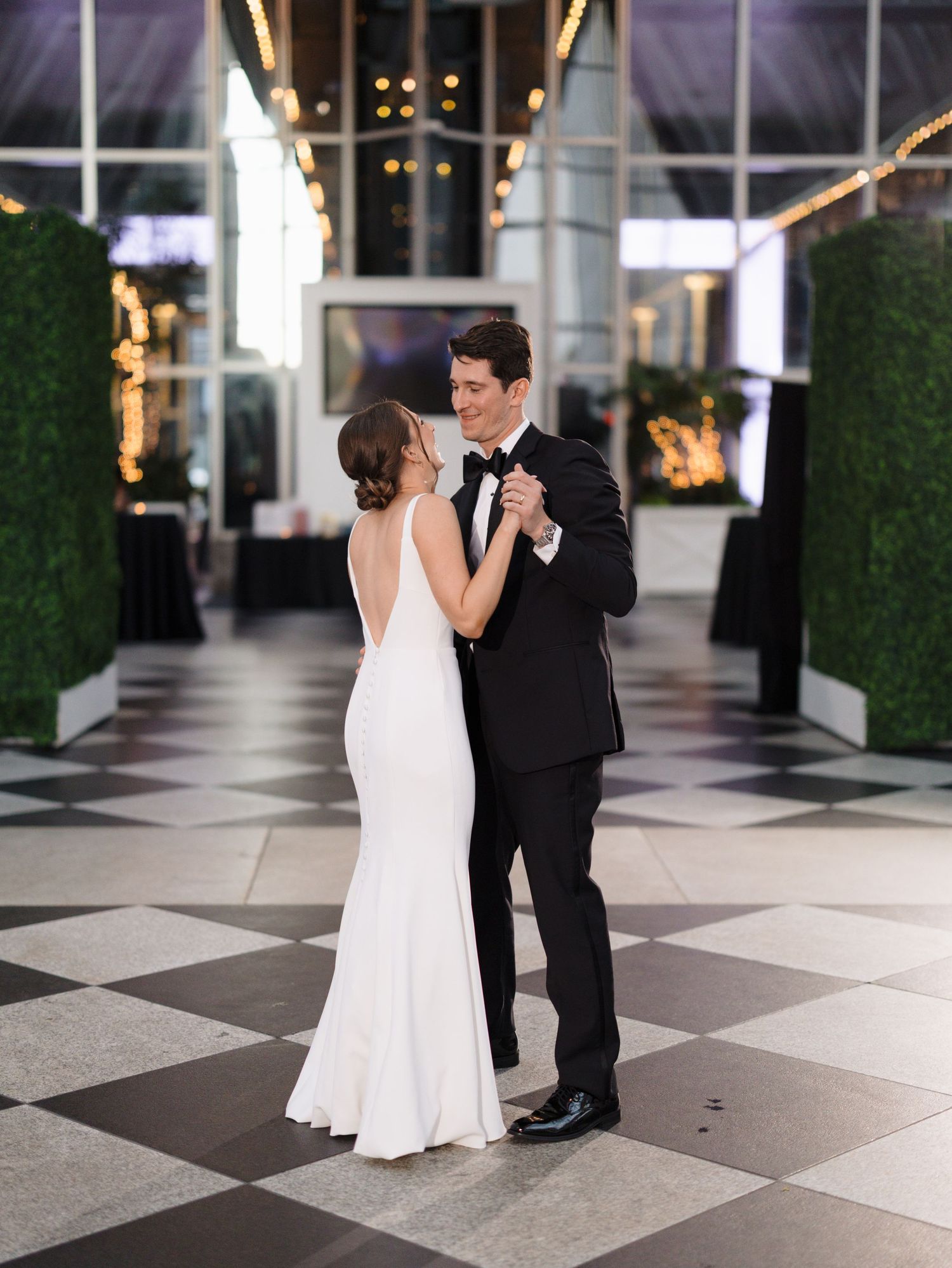 A couple shares their first dance on a black and white checkered floor at their wedding reception.